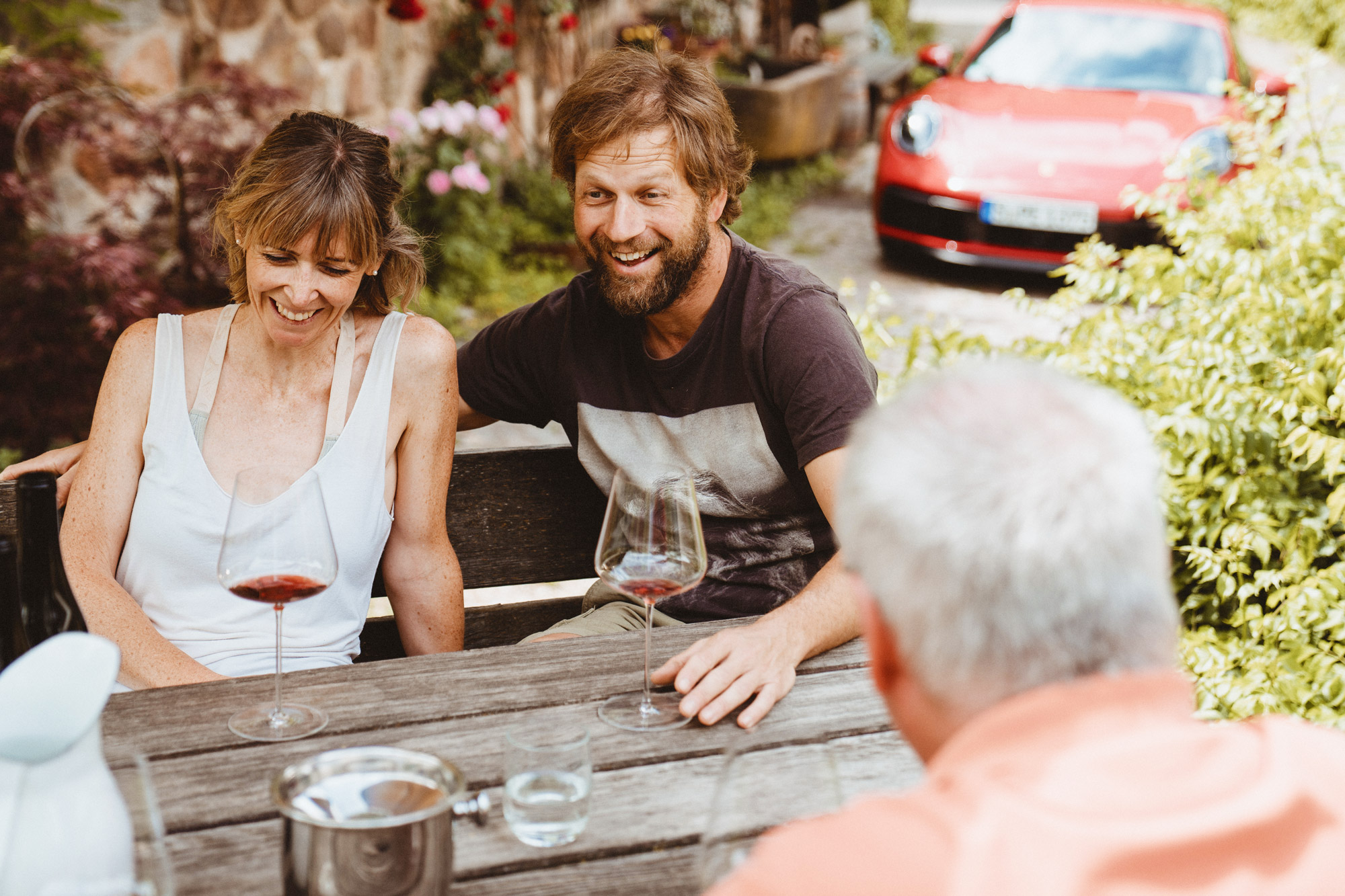 People sitting at wooden table, red Porsche 911 in background