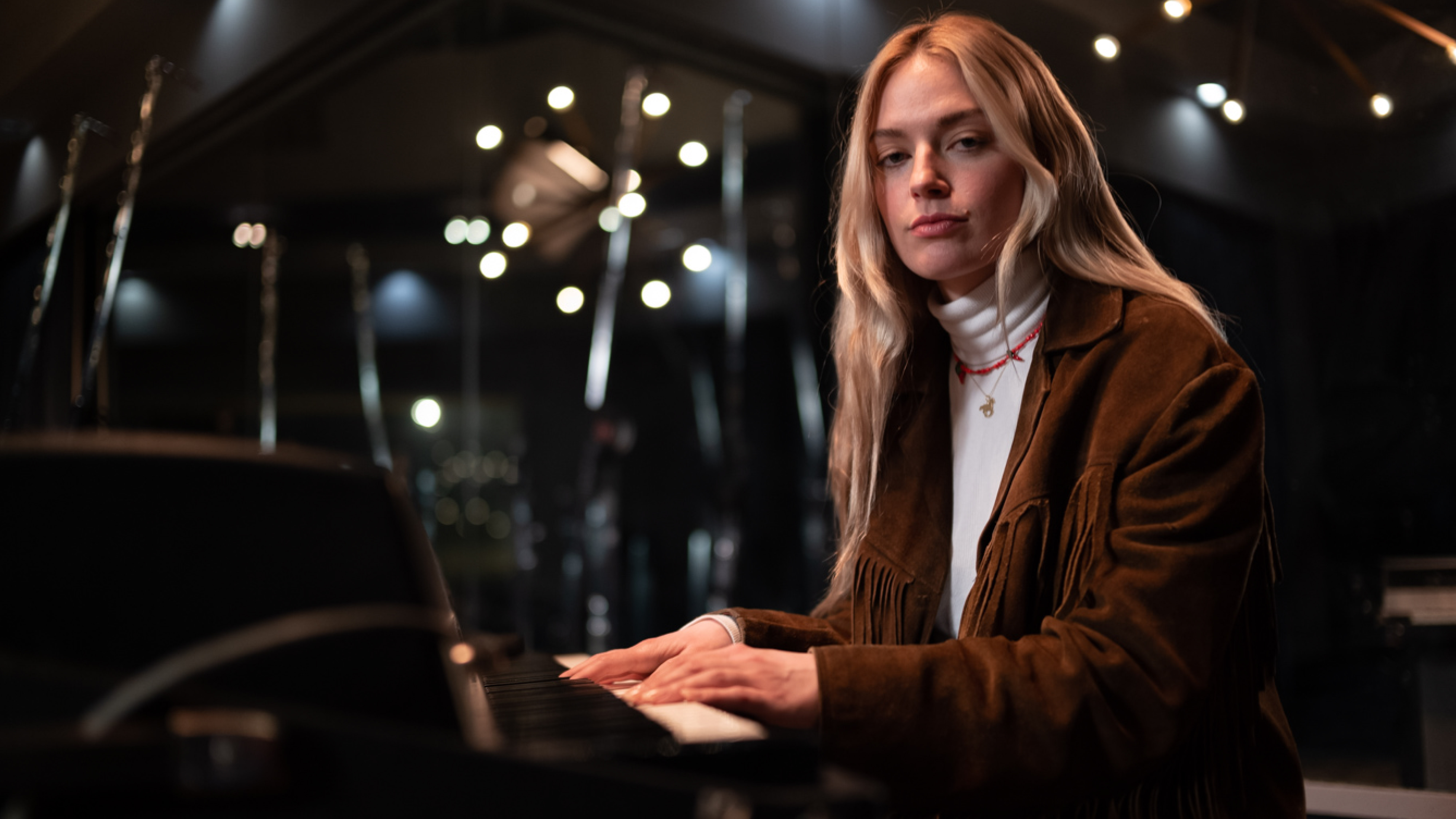 Blonde-haired woman looks at camera while playing piano 