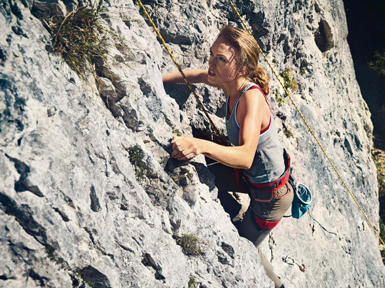 Woman attached to guide ropes climbs up a rock face