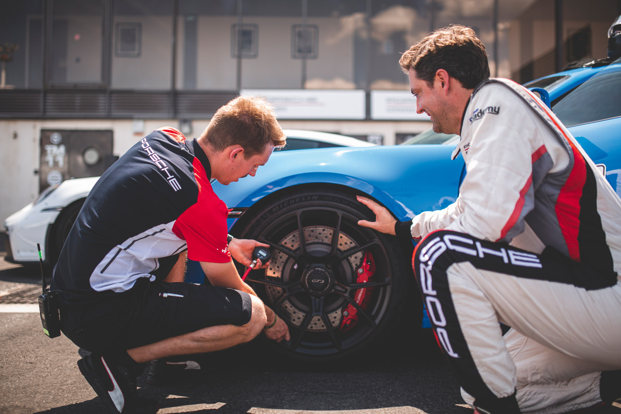 Two men checking tyre pressure on blue Porsche 911 GT3