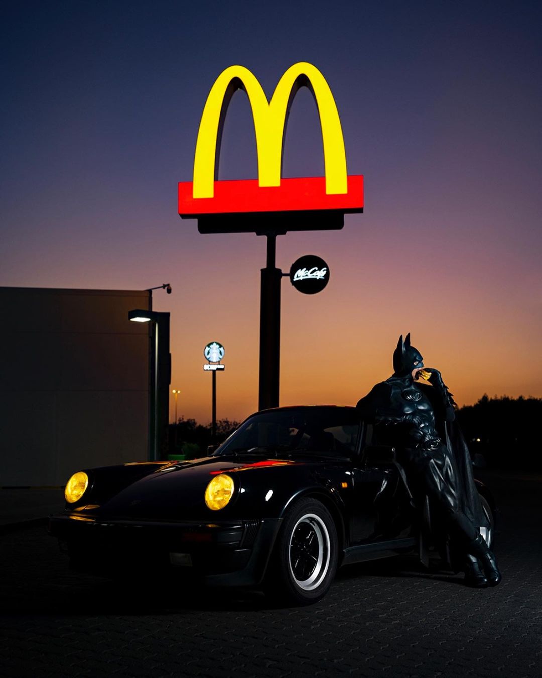 Batman eats burger leaning against 911 (930) Turbo outside McDonalds