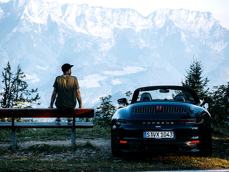 Man looking at mountains besides black Porsche 911 Cabriolet