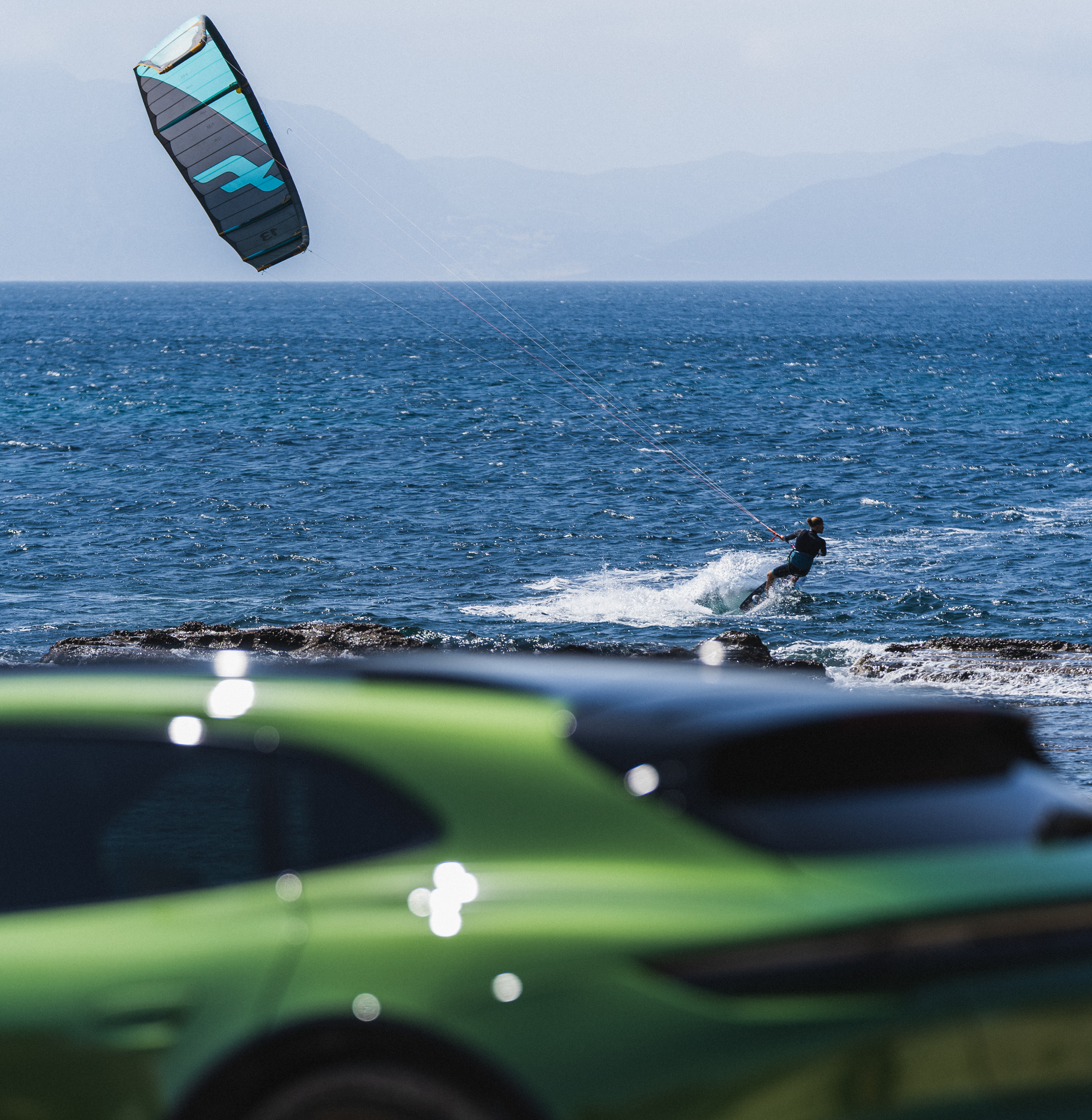 Kitesurfer riding waves, green Porsche in foreground