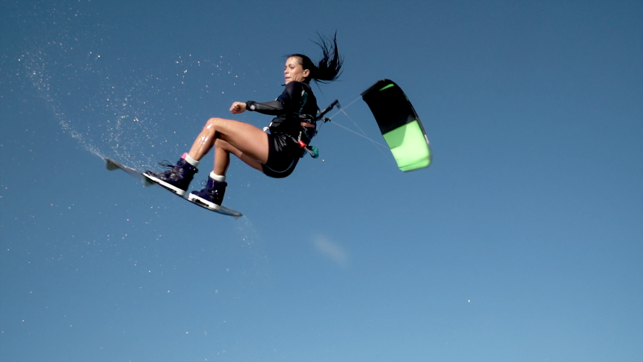 Woman flying high on kitesurfing board, kite visible above her