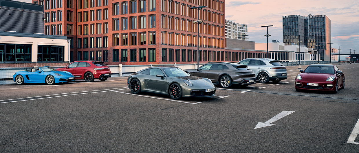 Six Porsche models in car park outside tall office buildings