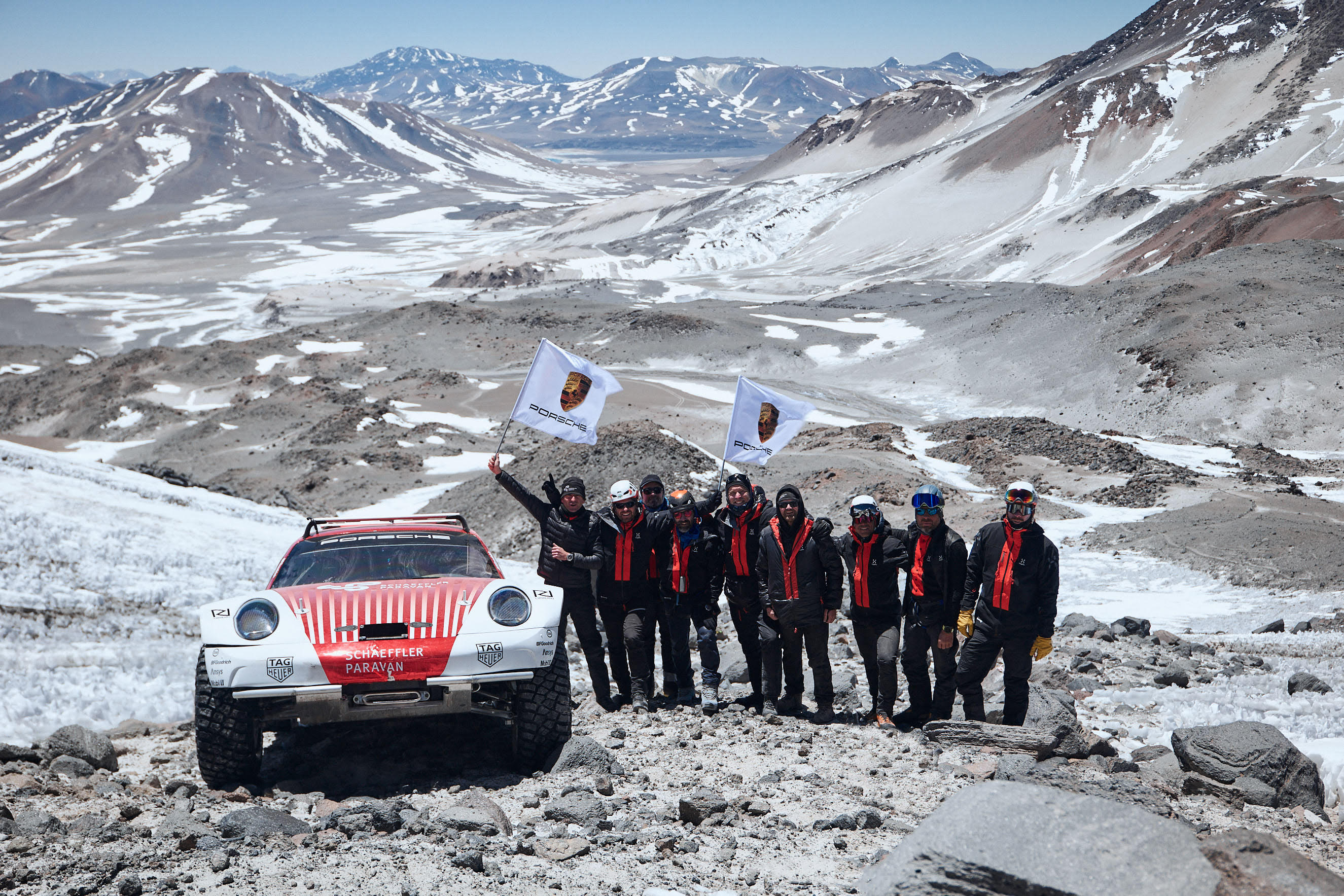 Nine people standing next to off-road Porsche 911 on volcano