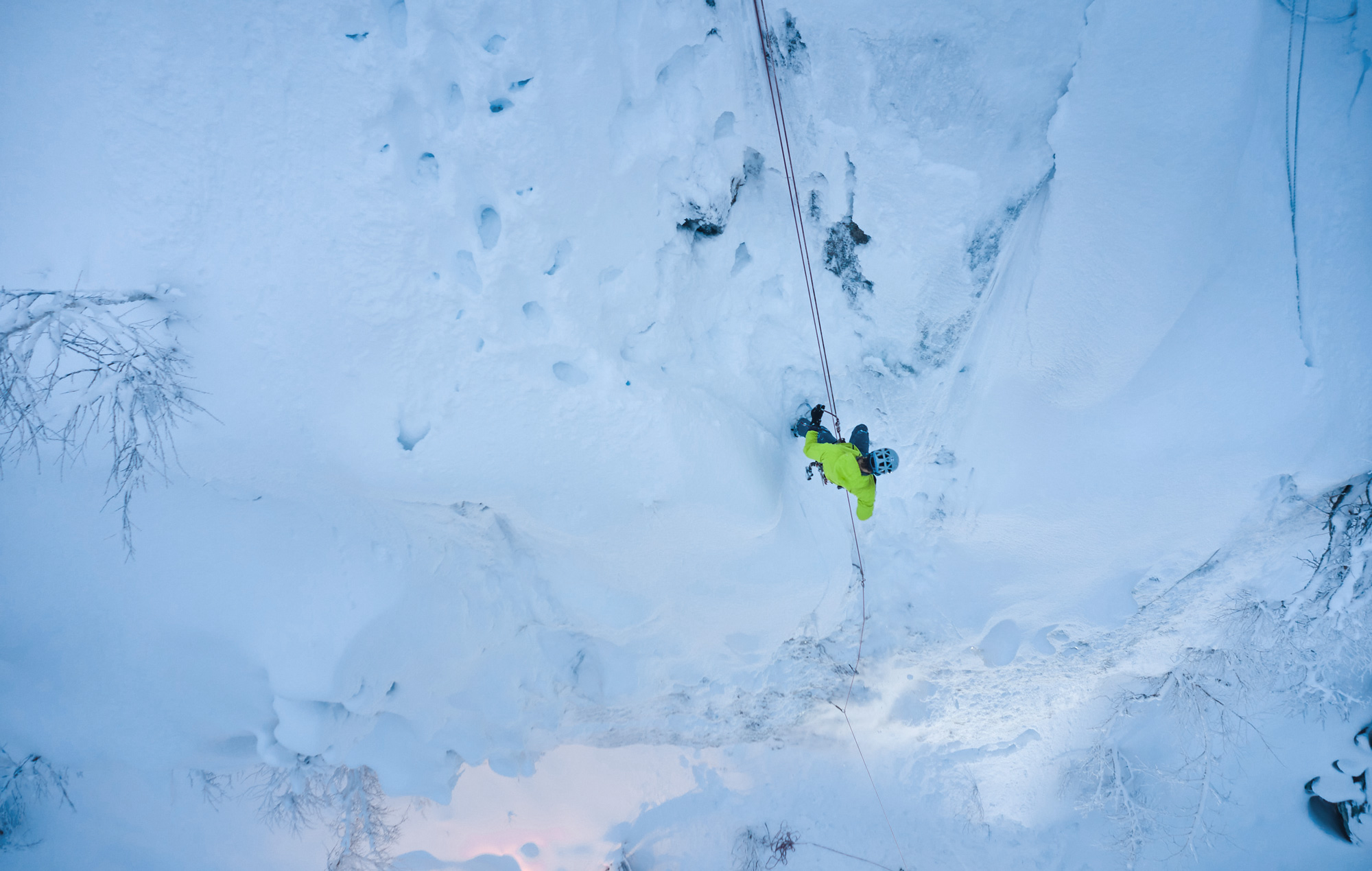 Bird's eye view of an ice climber. Ice climber hangs on the rope and climbs an ice wall