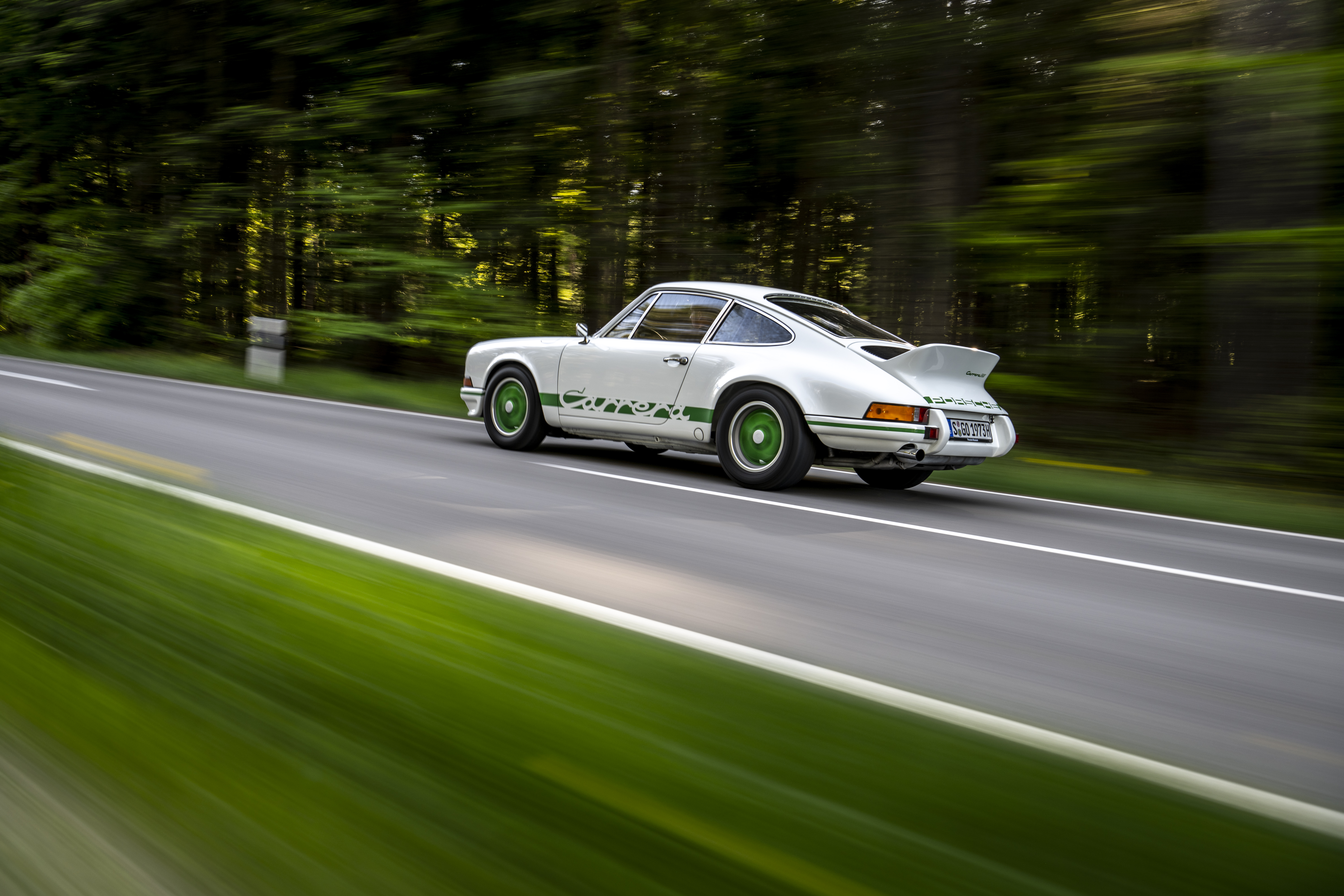 Porsche 911 Carrera RS 2.7 driving on a tree-lined road