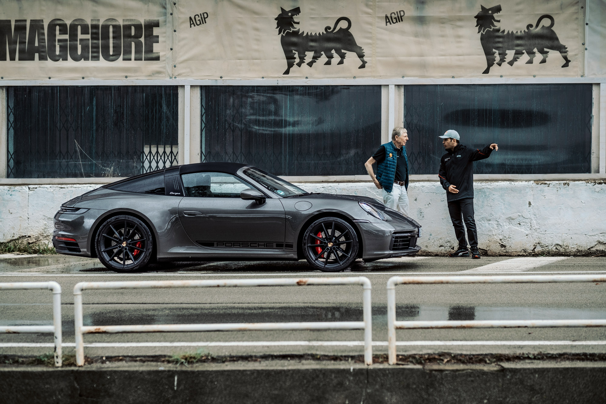 Two men standing next to silver Porsche 911 Targa