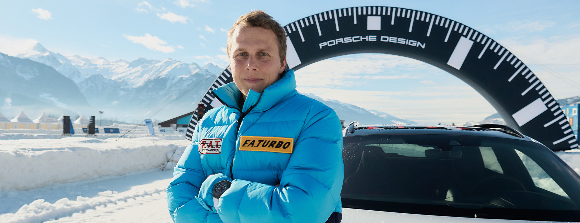 Man crossed arms leaning on Porsche in snow, mountain backdrop