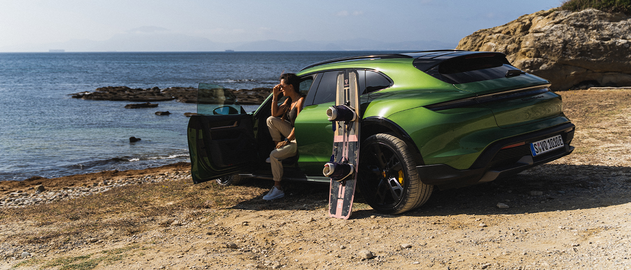 Woman sat in green Porsche, kitesurf board leaning against it