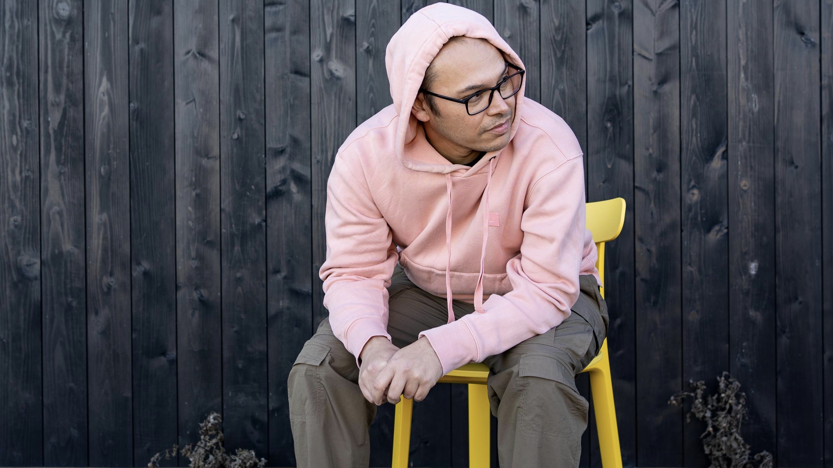 Artist Chris Labrooy sitting, wearing pink hoodie