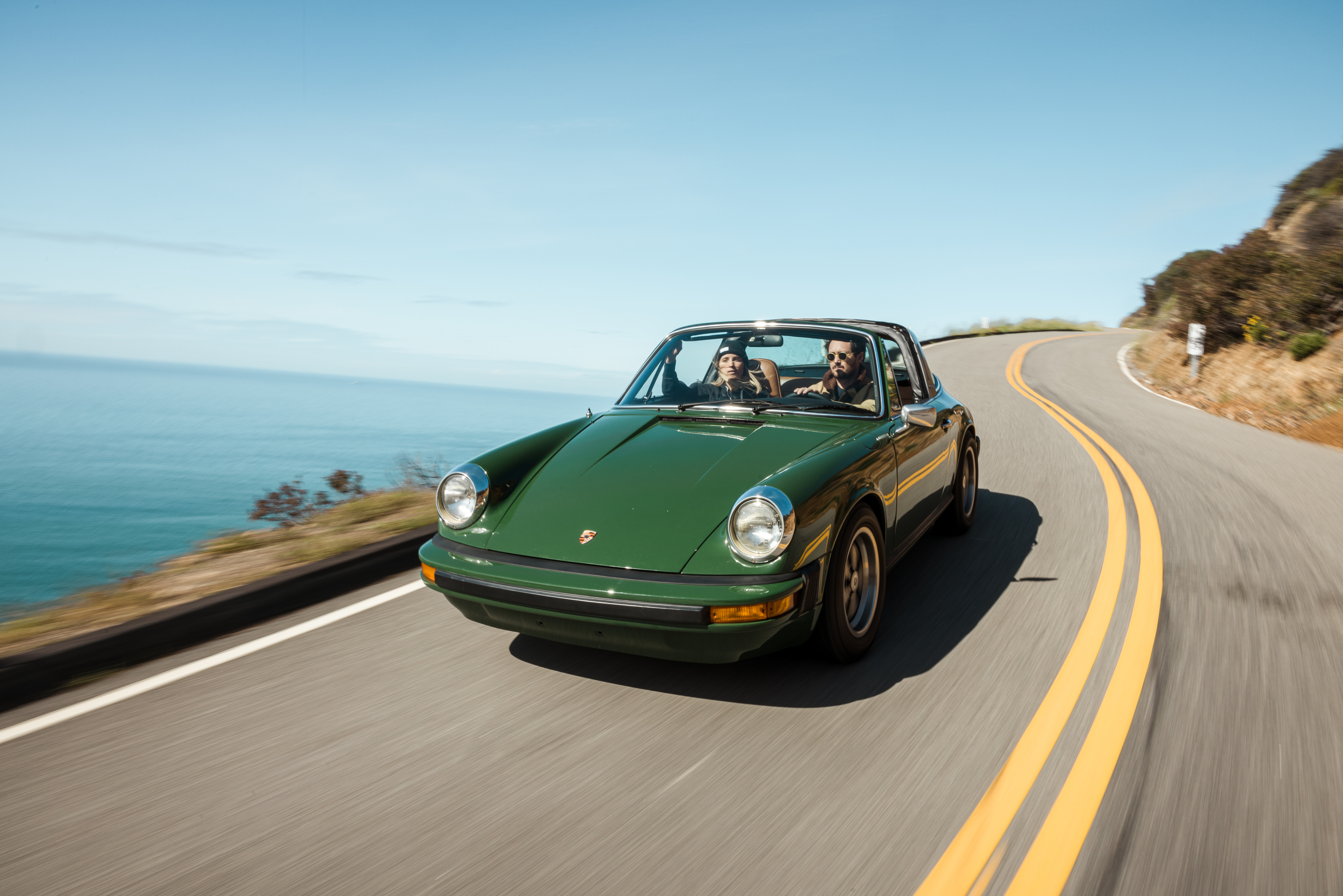Green Porsche 911 Targa driving down coastal Californian road