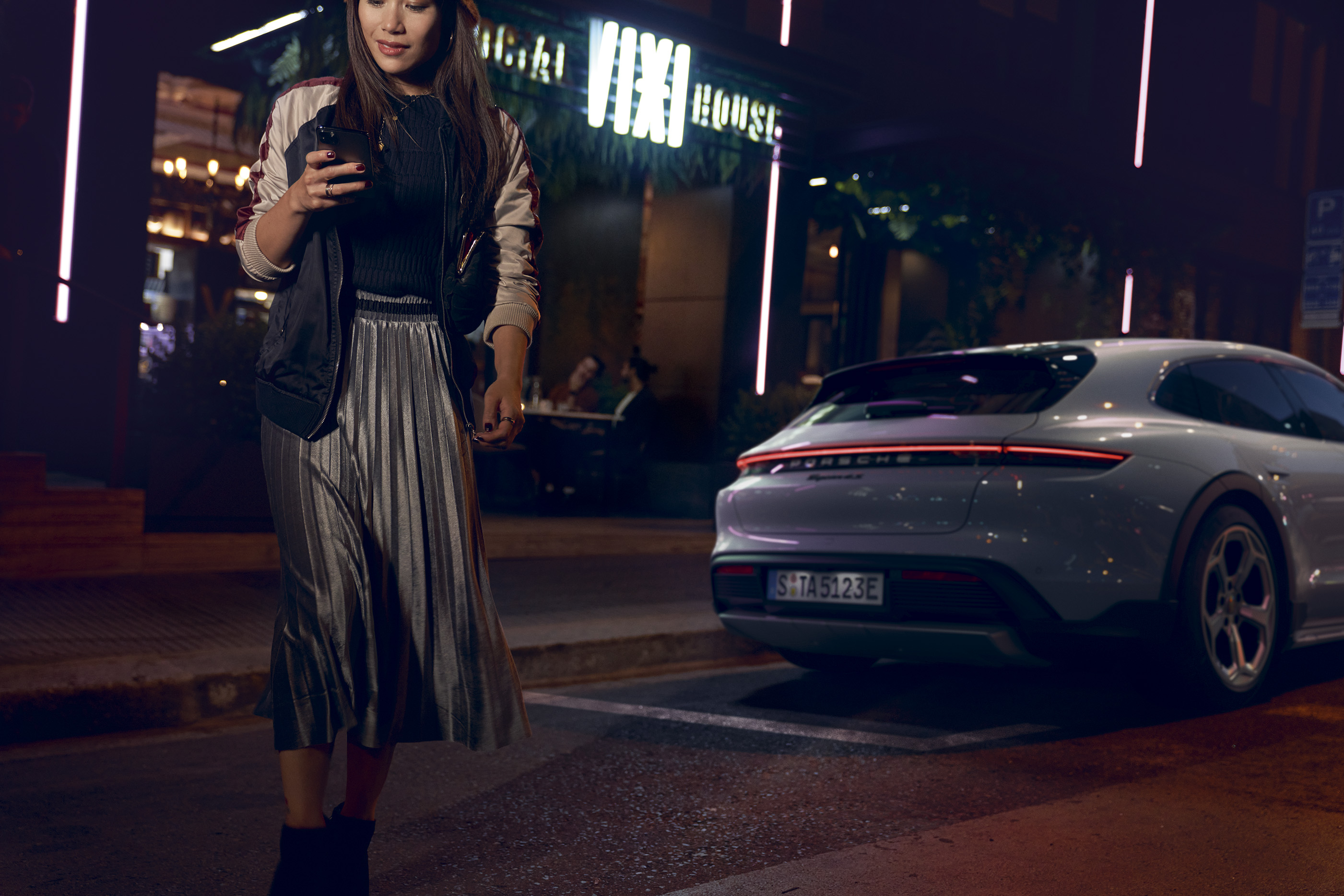 Woman walking across street at night, Porsche car behind