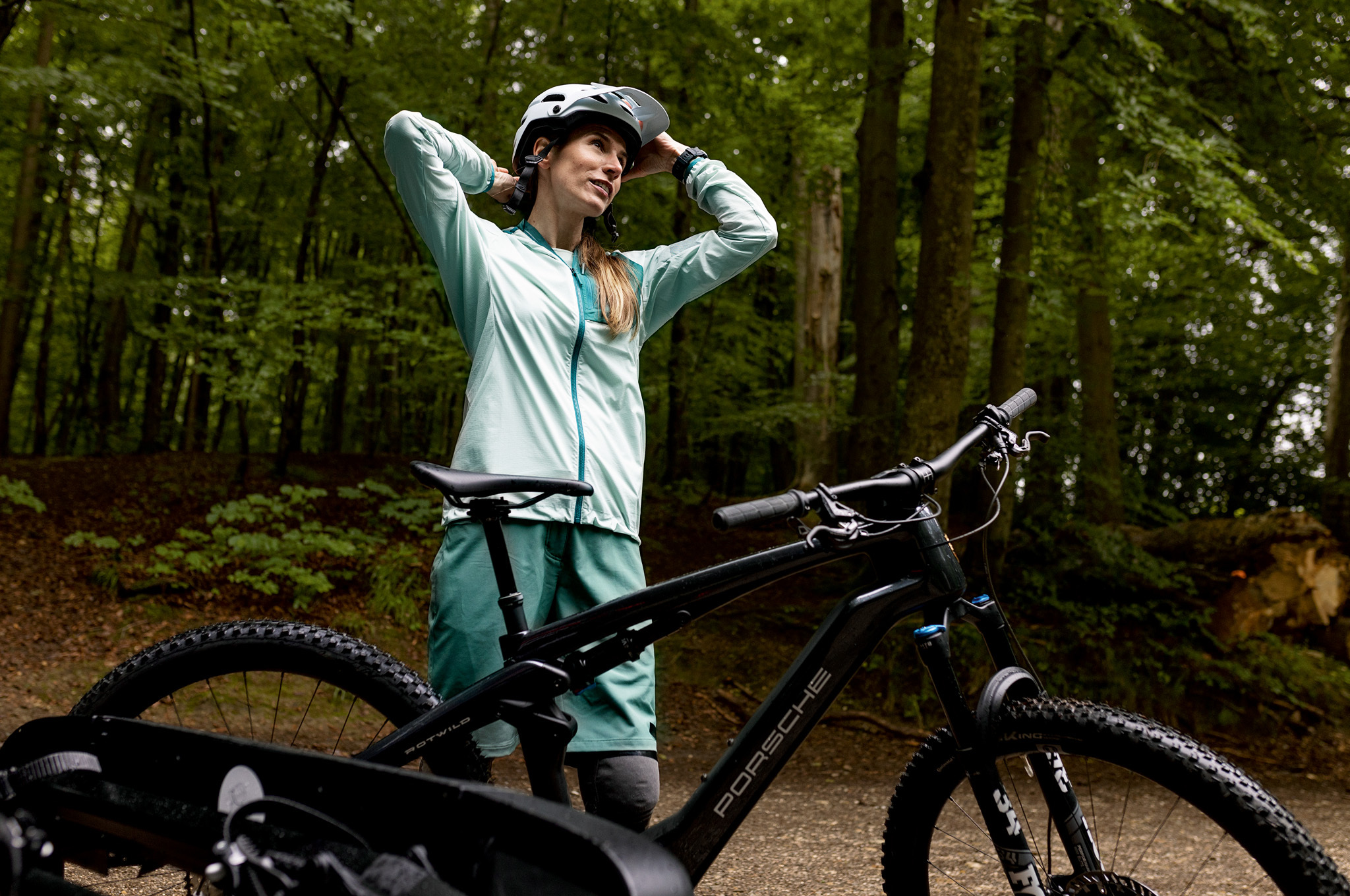 Woman in mountain biking clothes in woods with Porsche eBike
