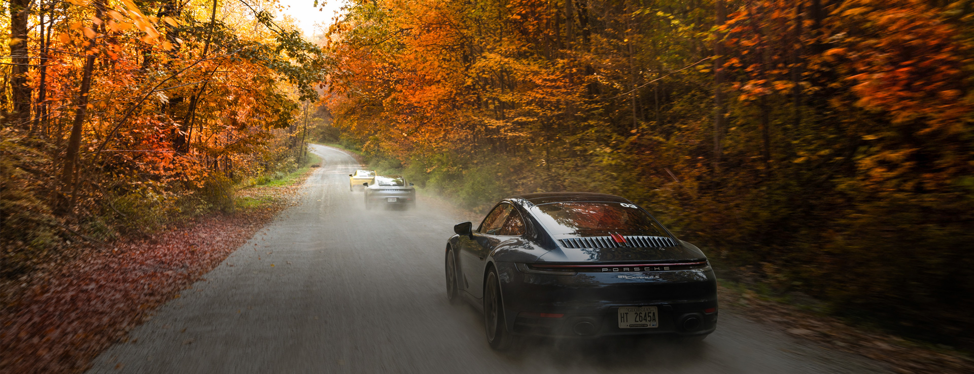 Three Porsche 911s driving through beautiful autumn forest