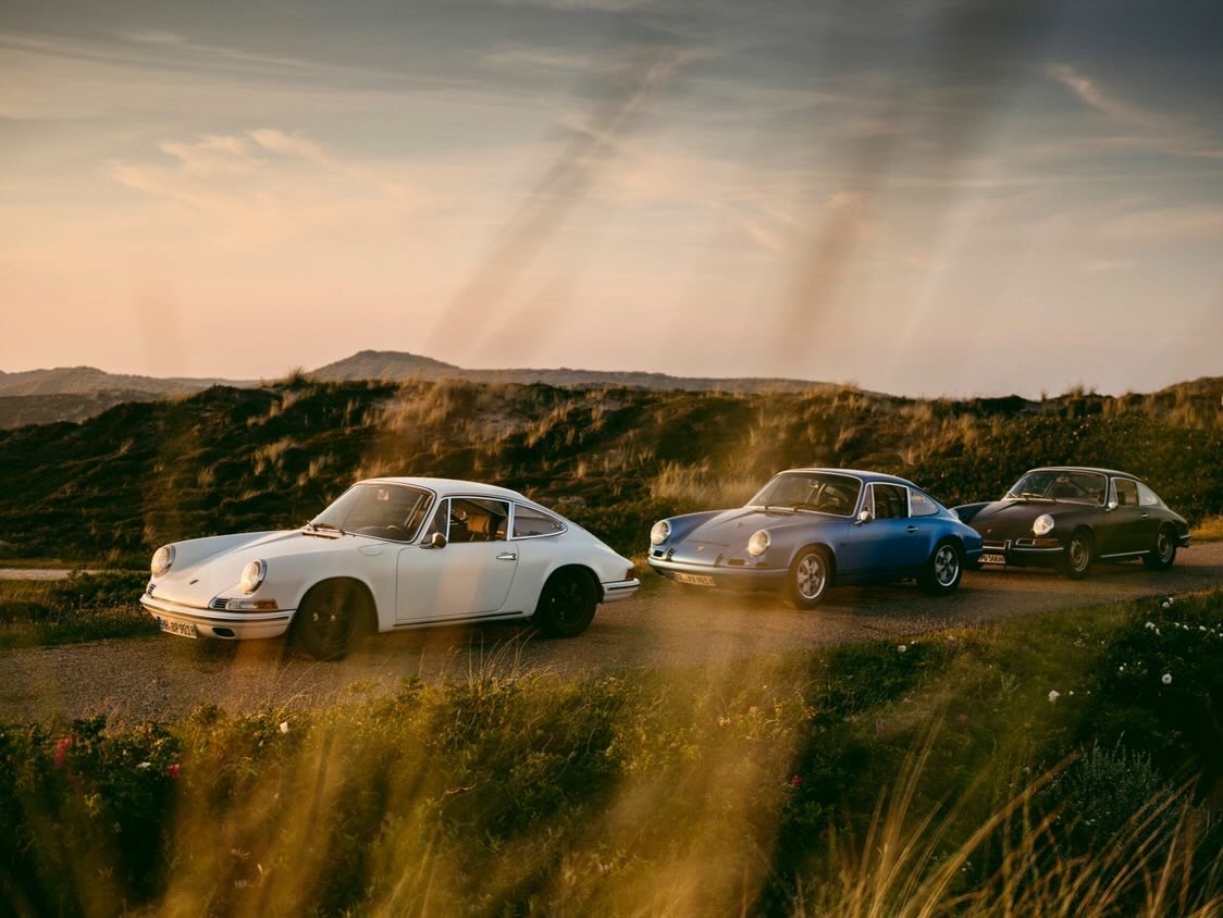 Three classic Porsche 911 sportscars on road in evening sunlight