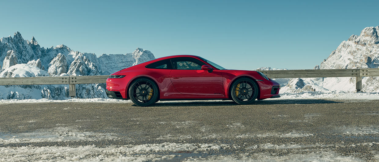 Red Porsche 911 GTS parked, snow-covered mountains behind