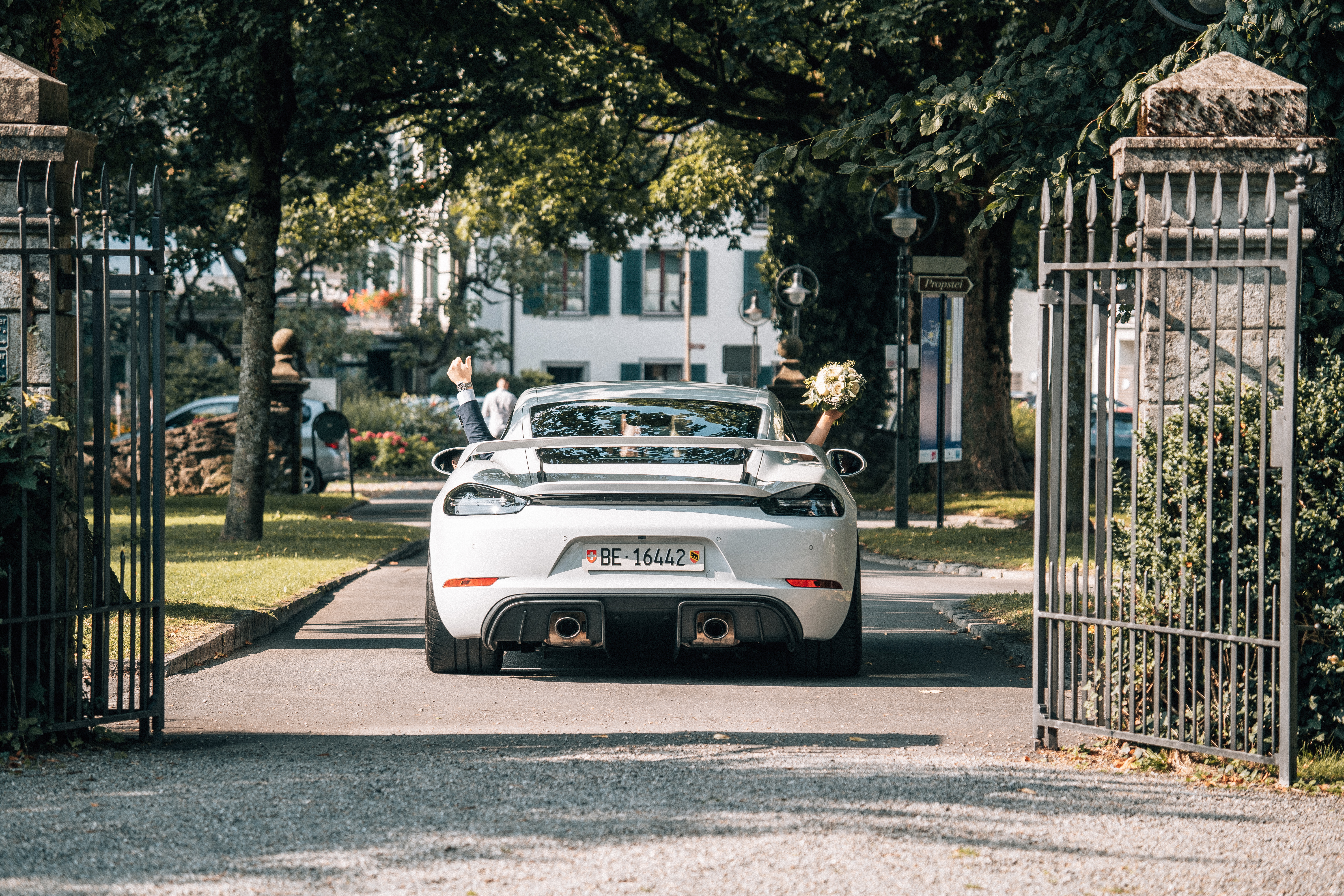Married couple wave from white Porsche 718 Cayman GT4
