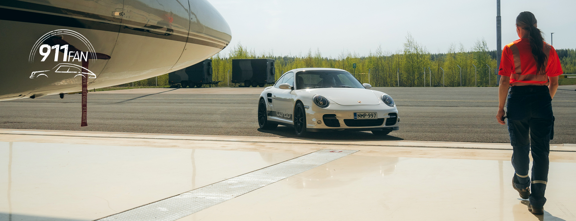 Woman walking towards white Porsche 911 with aeroplane in hangar