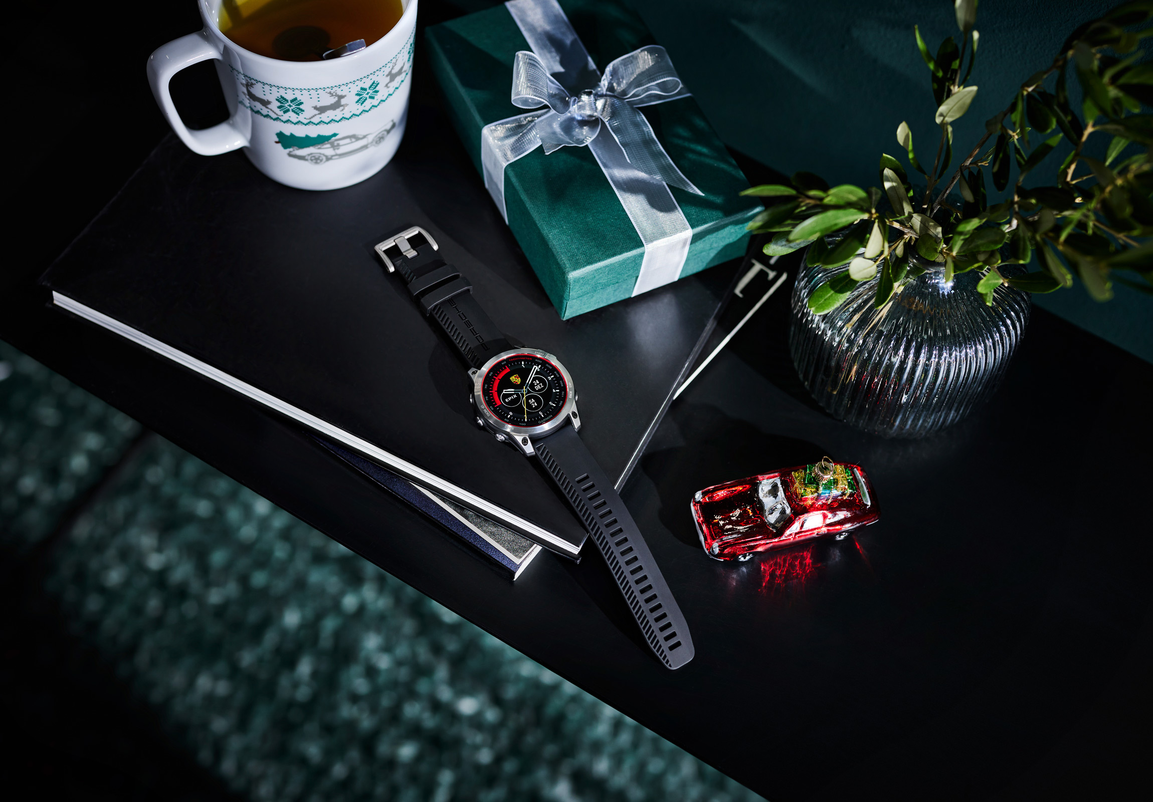 Porsche watch on table next to tea, wrapped present and model car