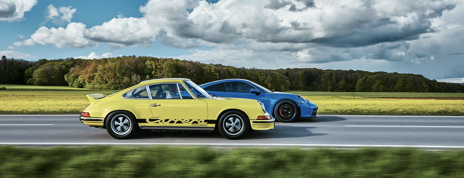 Two Porsche sportscars overtaking in front of yellow fields