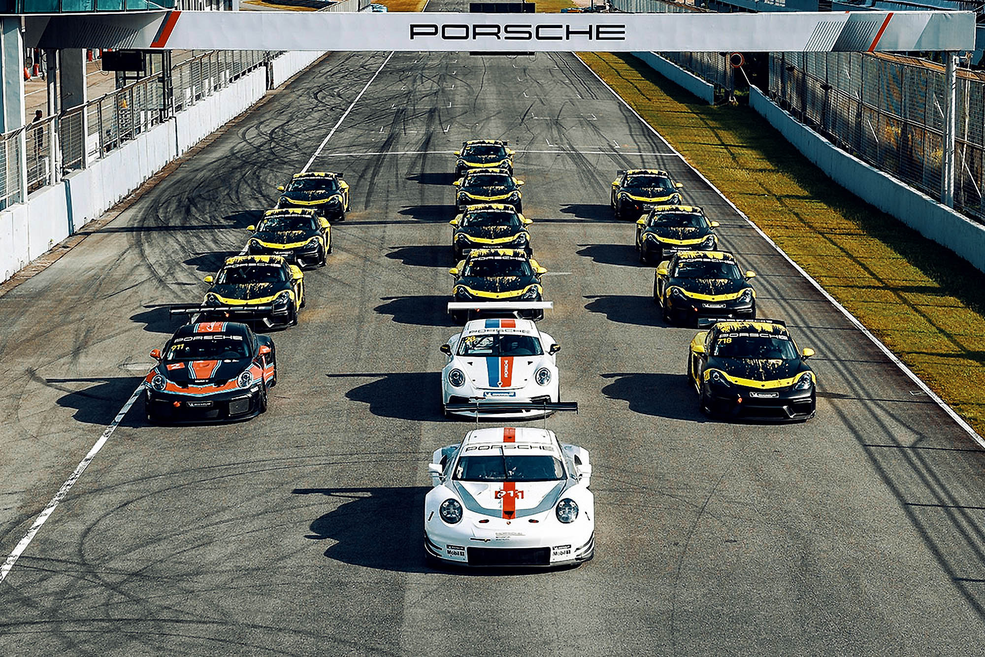 Three lines of Porsche cars on the starting grid of a track