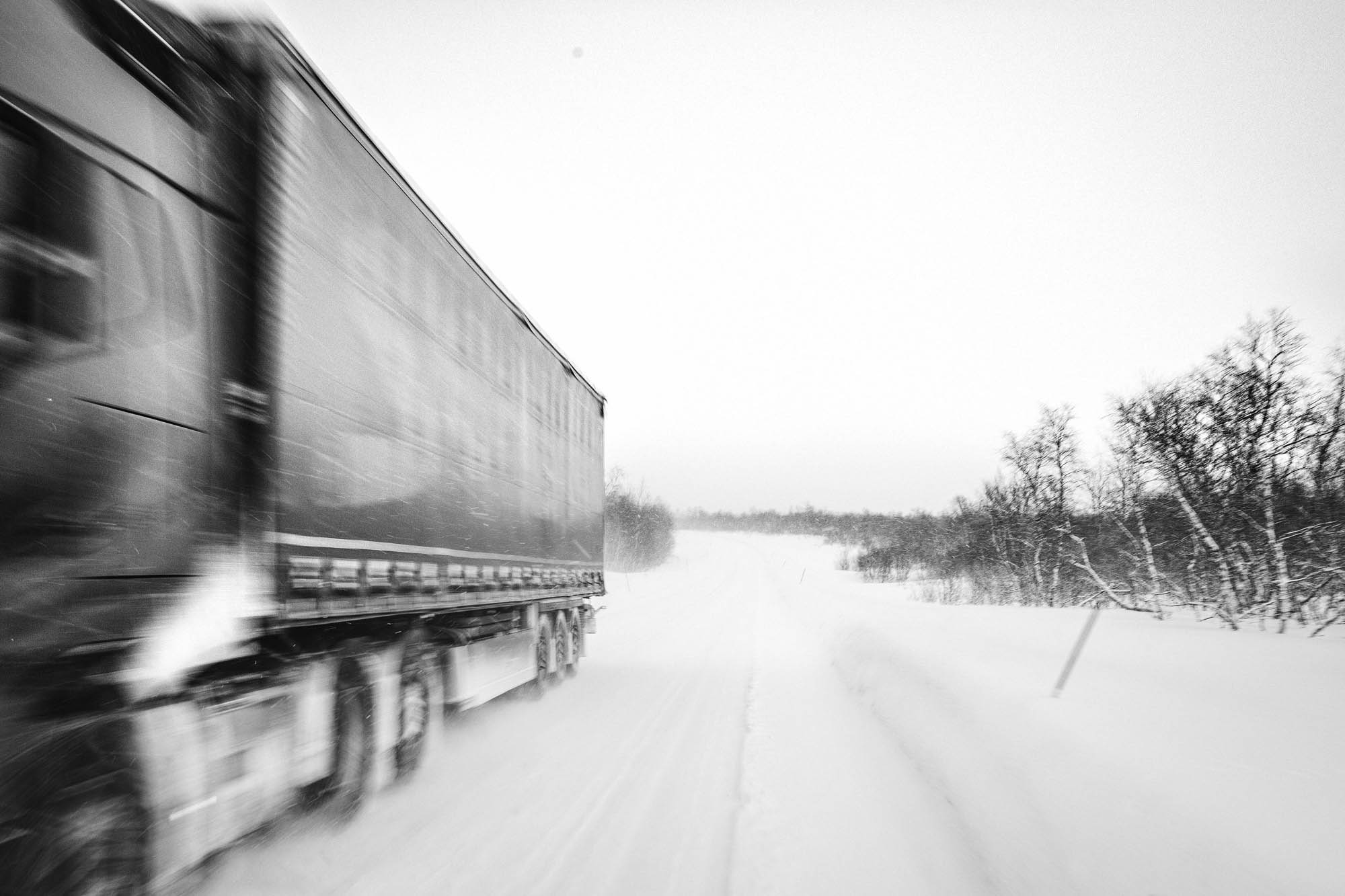 Large, 12-wheeler articulated lorry speeds into foreground, snowy road behind