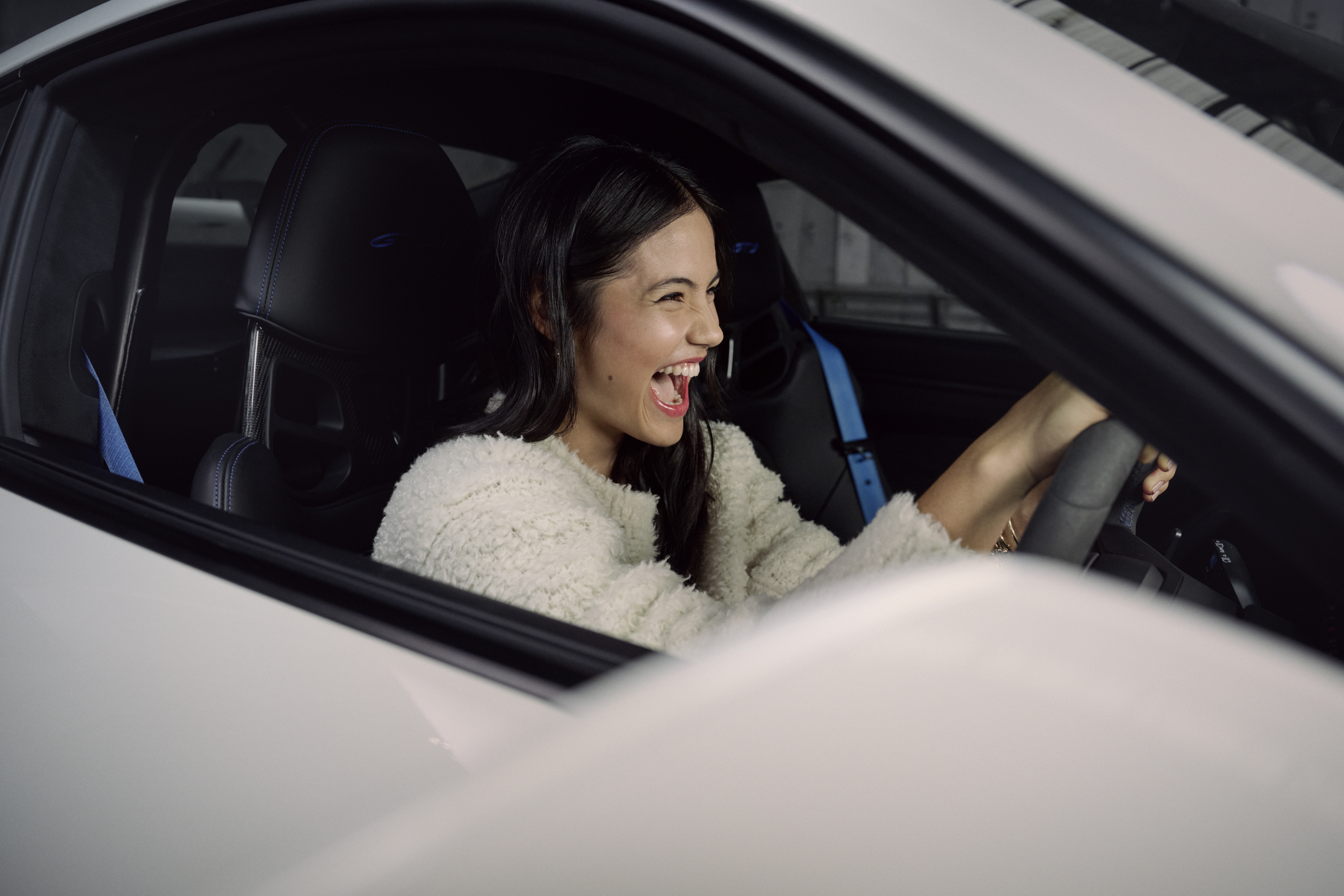 Woman laughing inside Porsche 911, hands on steering wheel