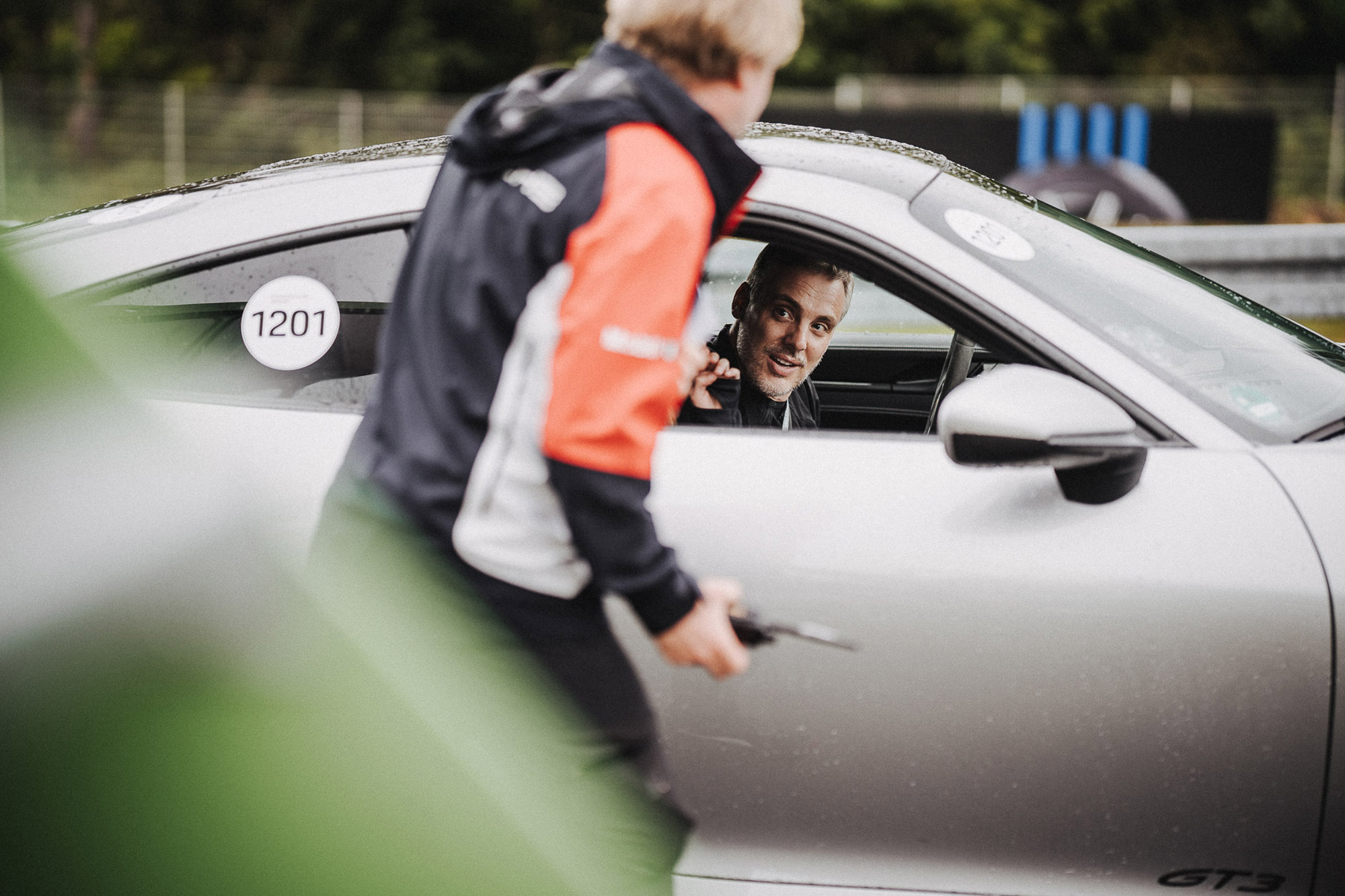 A Porsche instructor gives instructions to a participant who is sitting in a Porsche