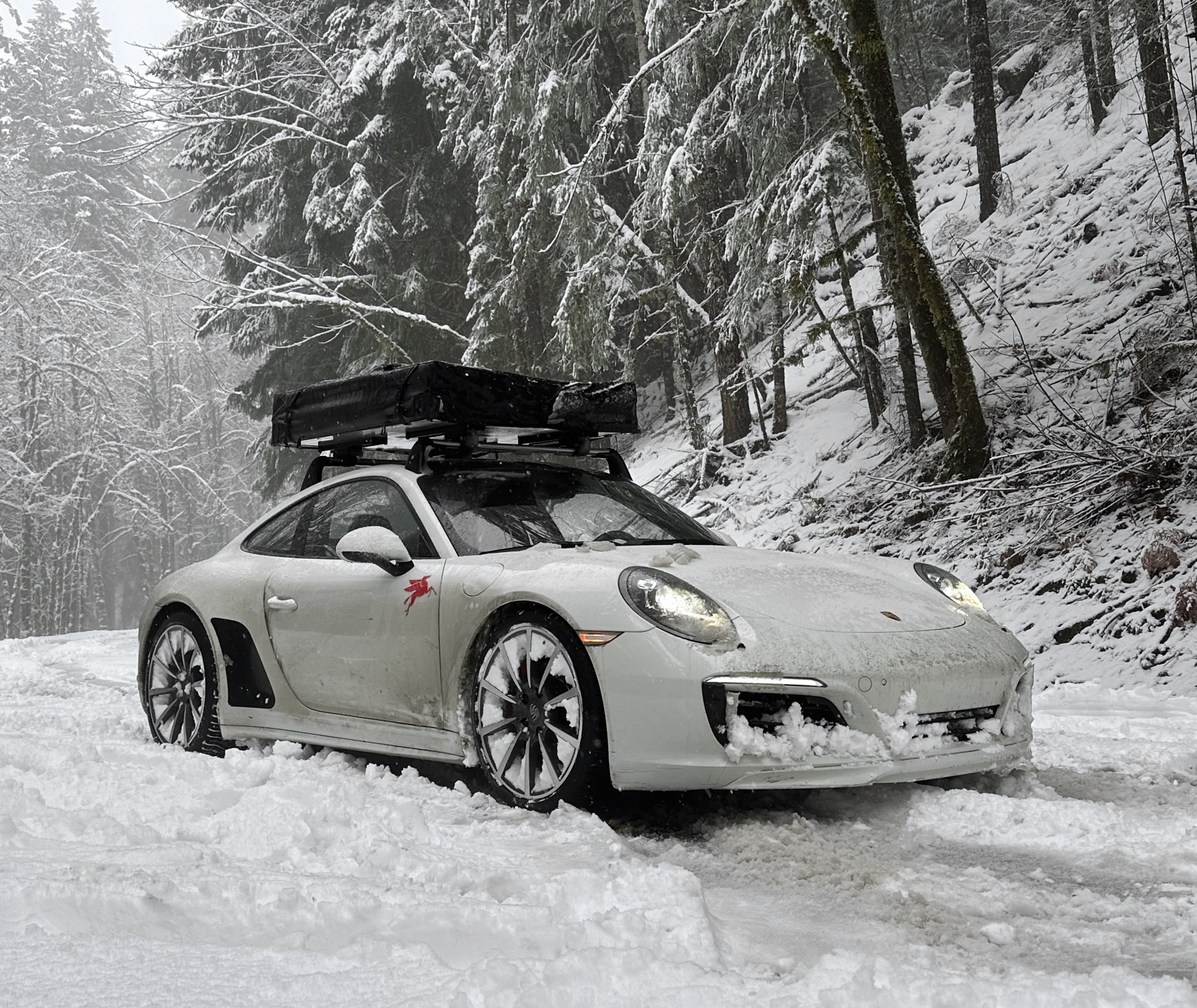 White Porsche 911 Carrera 4 in snow on mountain road