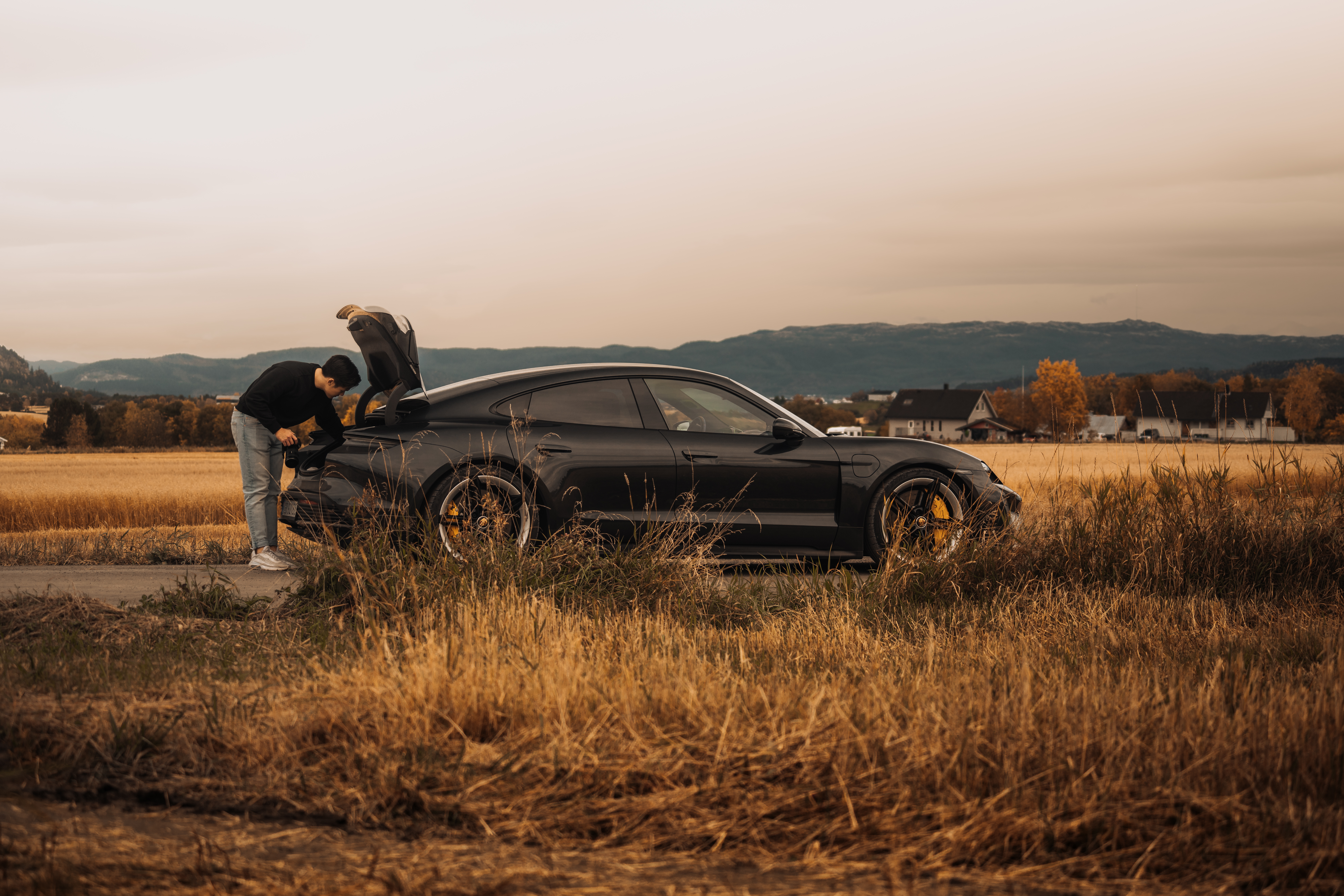 Man leaning into Porsche Taycan boot while parked in field