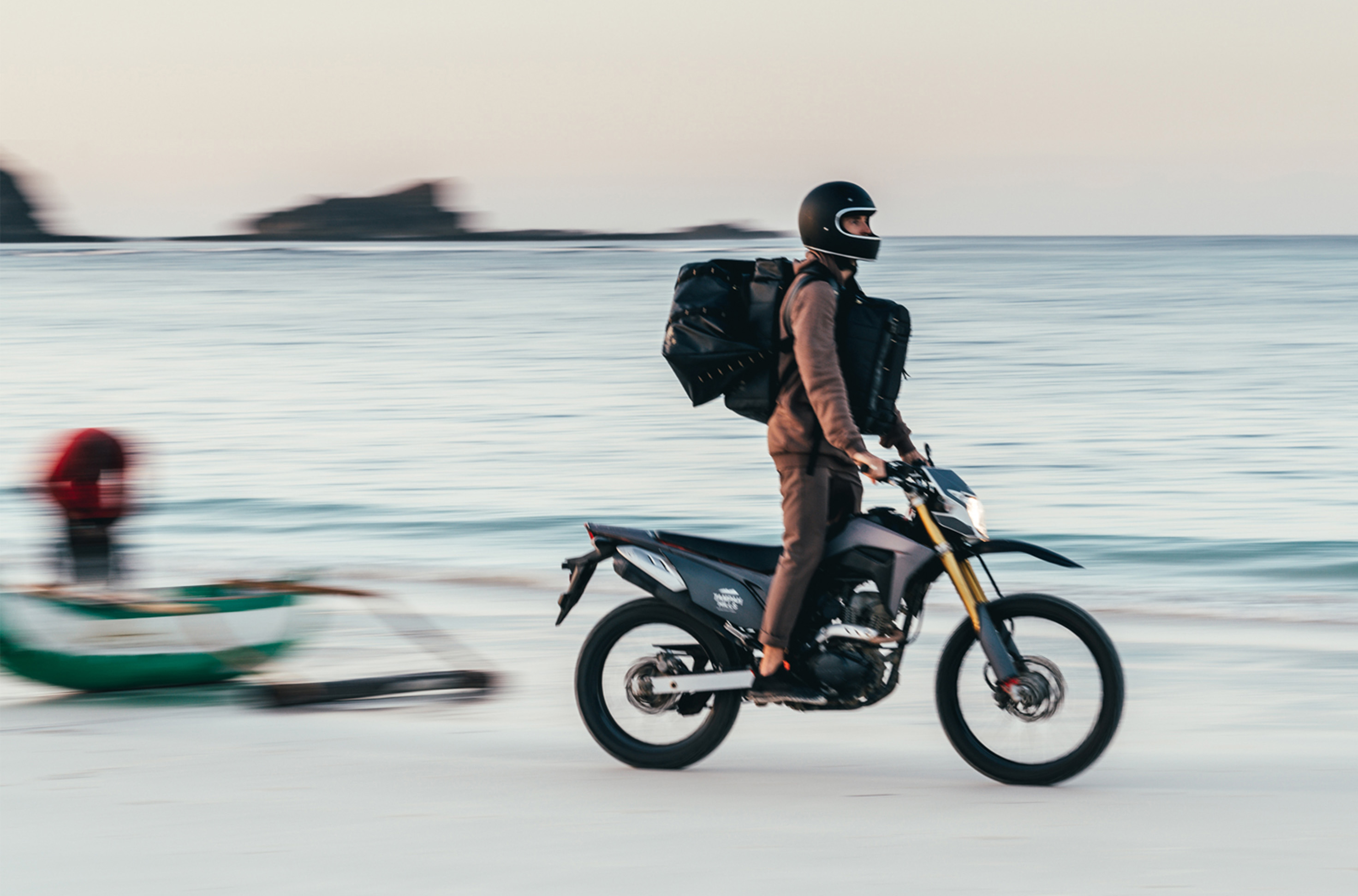 Man stands up on motorbike wearing camera bags on beach