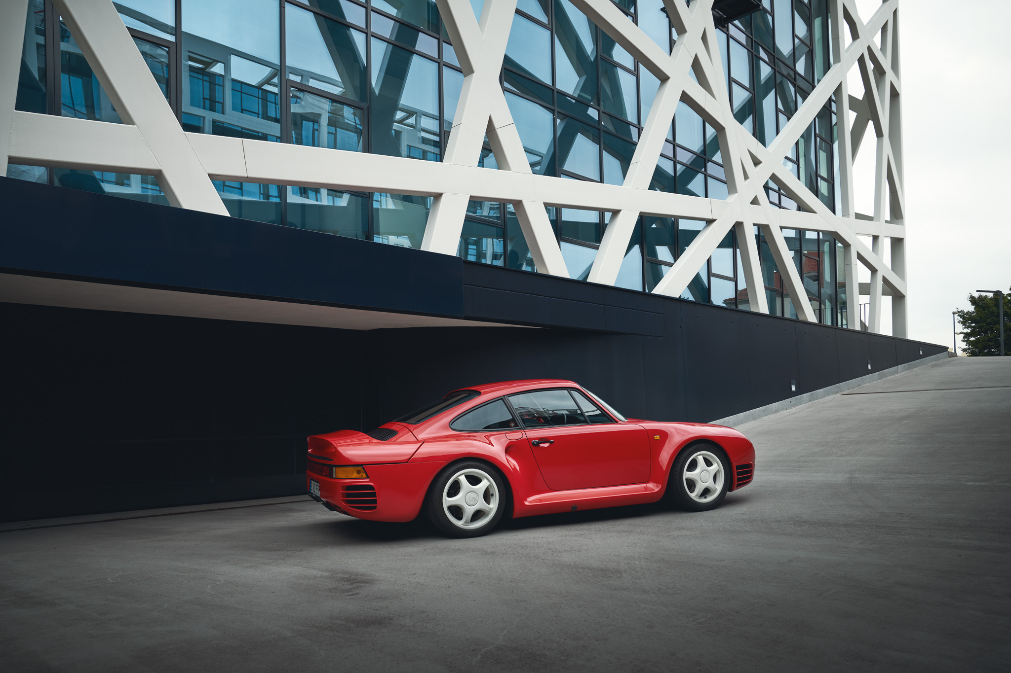 Red Porsche 959 production car driving past modern office building