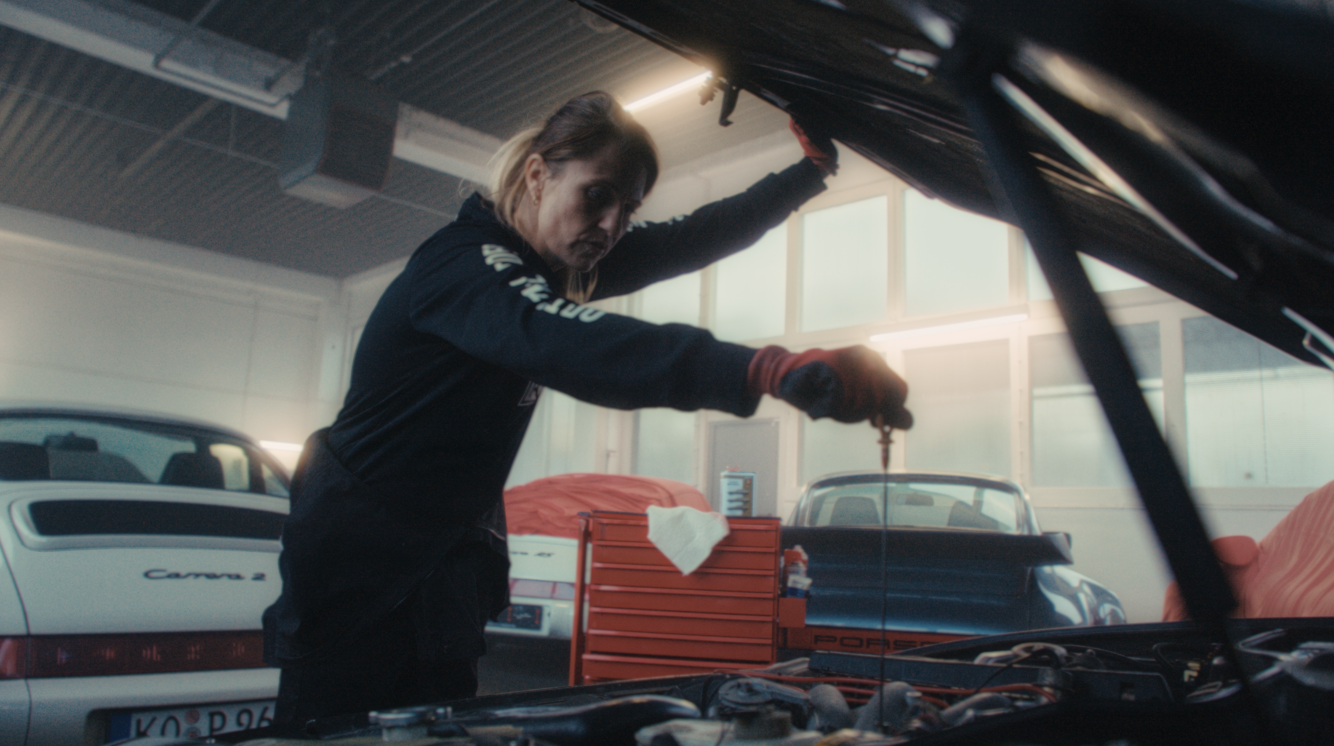 Woman inserts oil dipstick into engine of Porsche