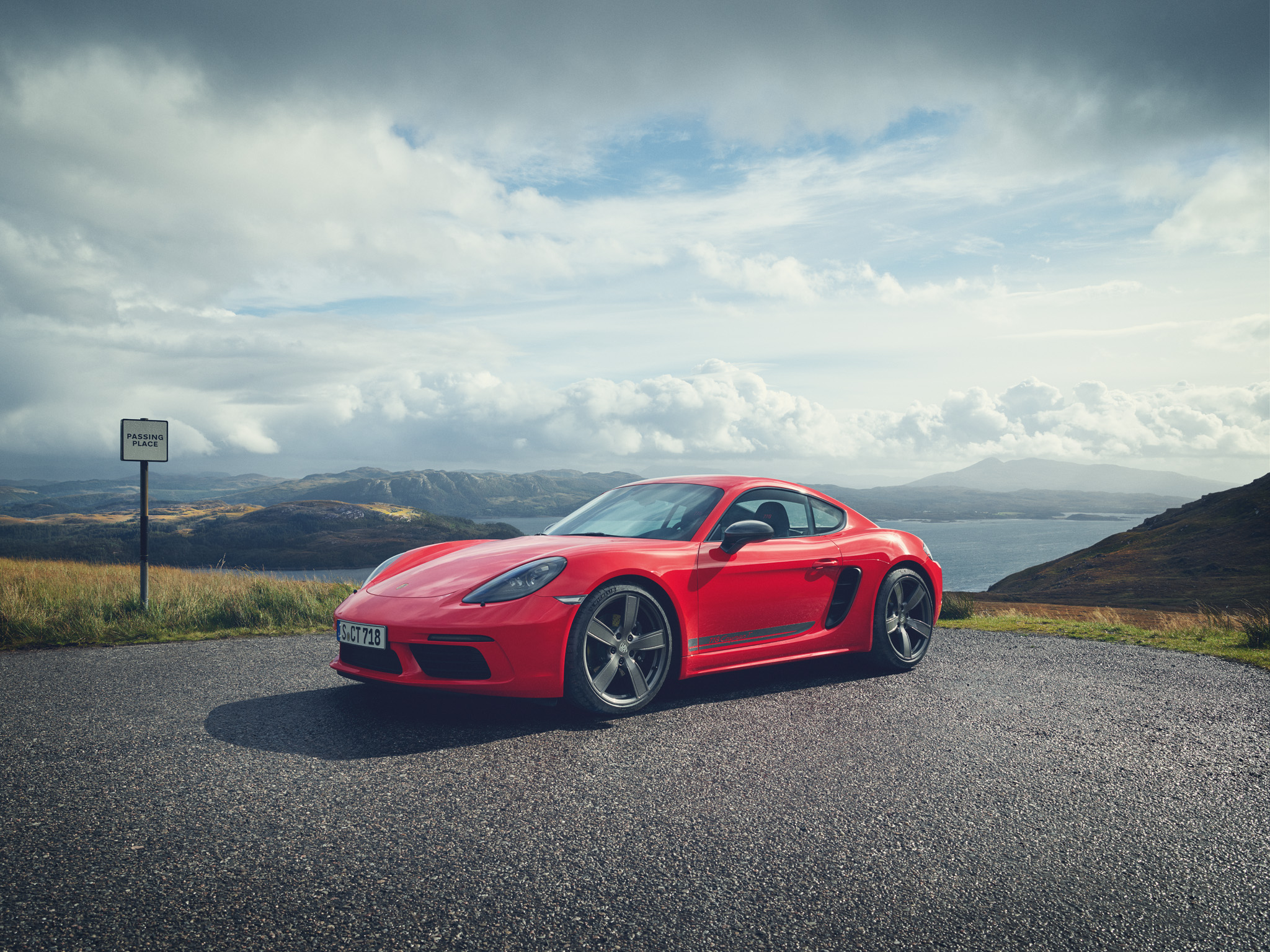Cayman in Guards Red parked with hills and water behind