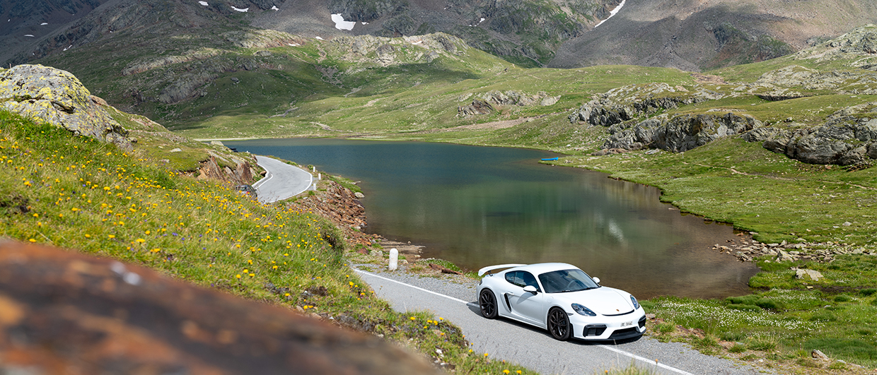 White Porsche 718 Cayman GT4 by lake in mountains