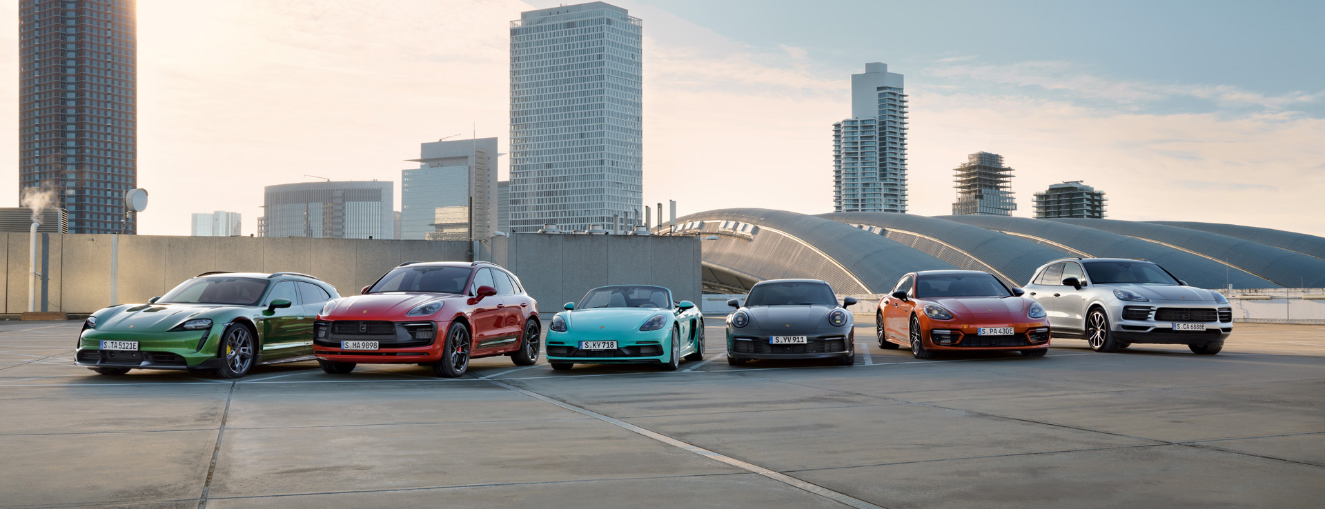 Six Porsche models in front of skyscraper skyline by day