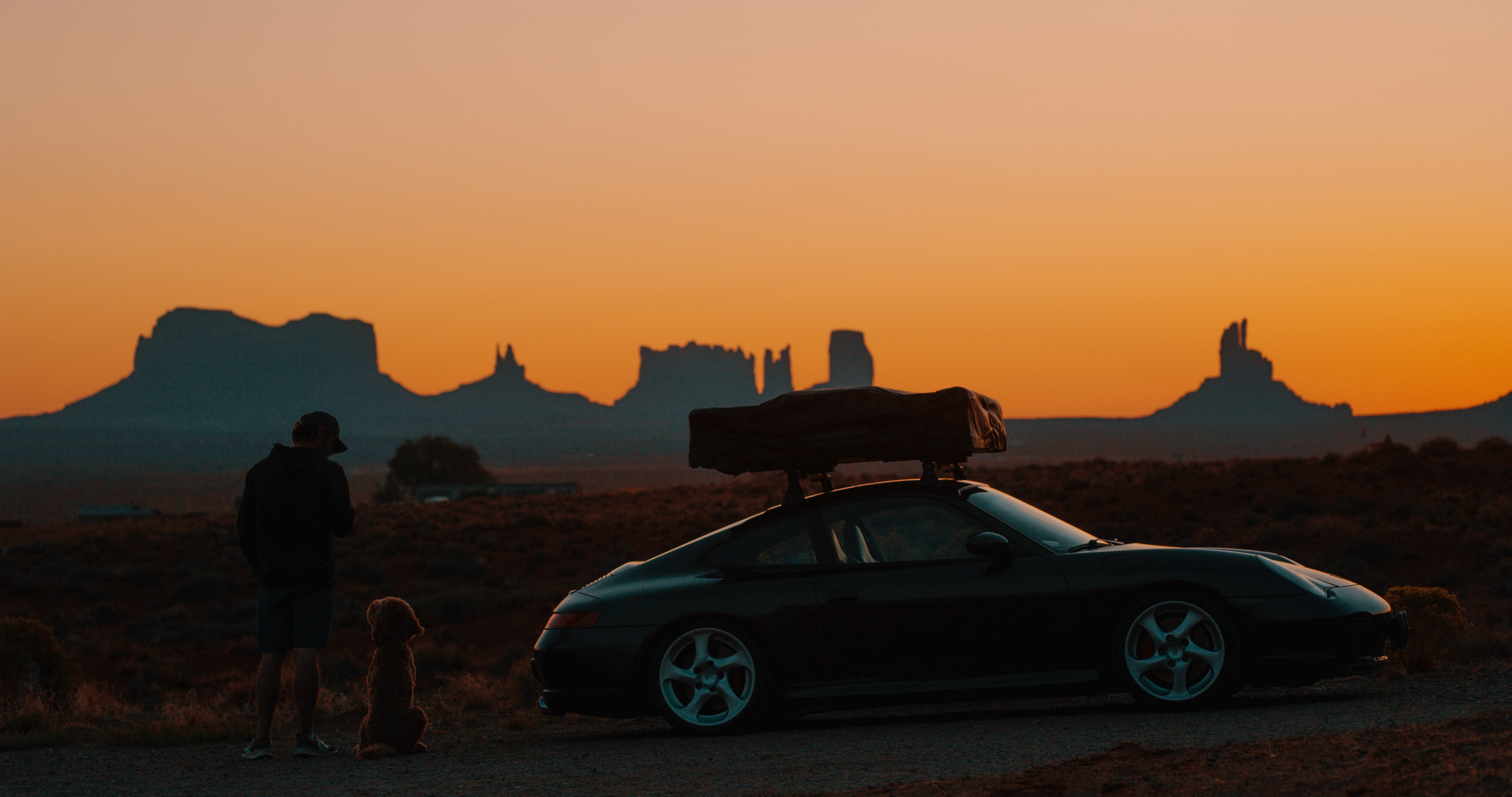 Man, dog and Porsche with roof tent against rocky Utah sunset