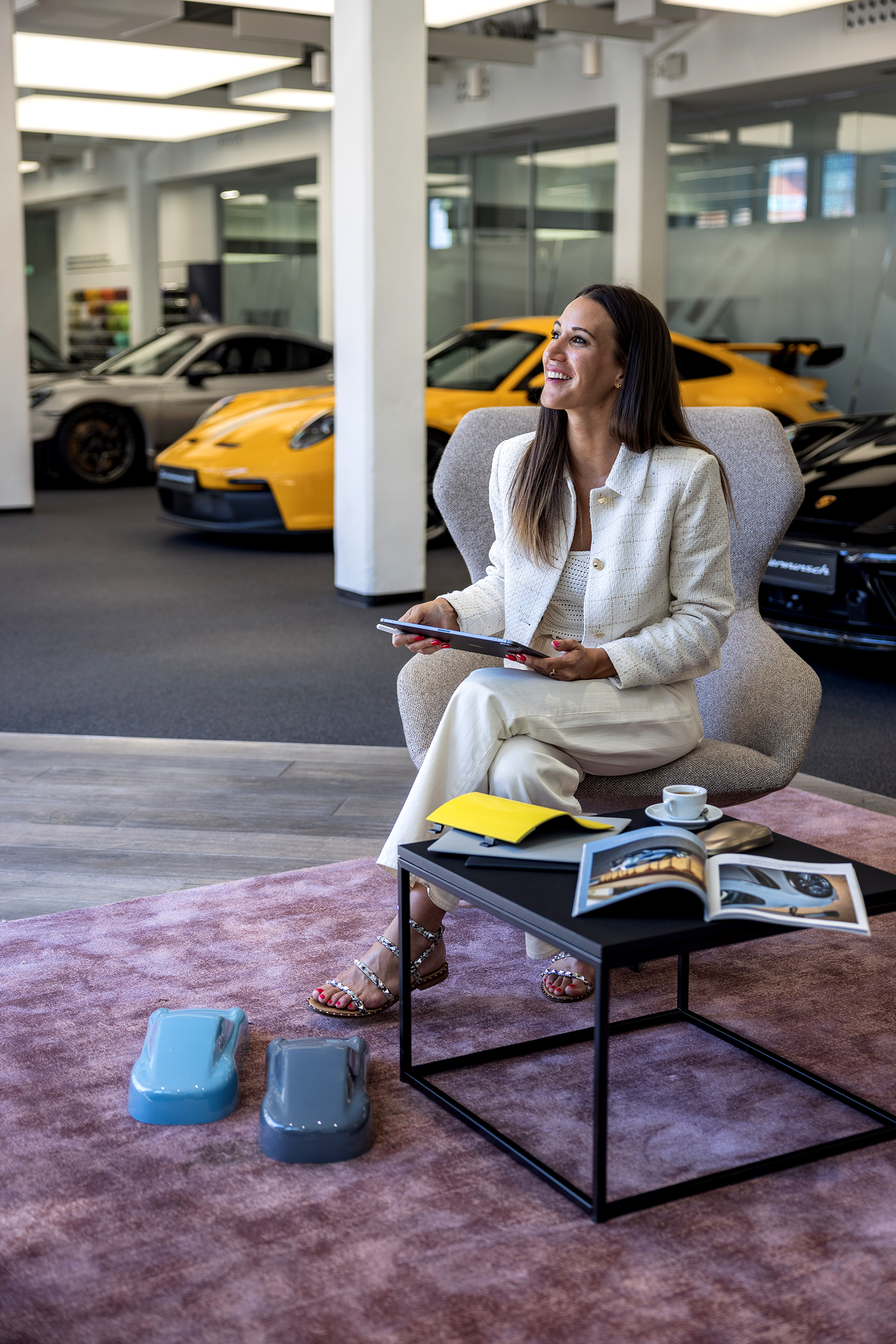 Woman sat in chair with iPad, Porsche cars behind her