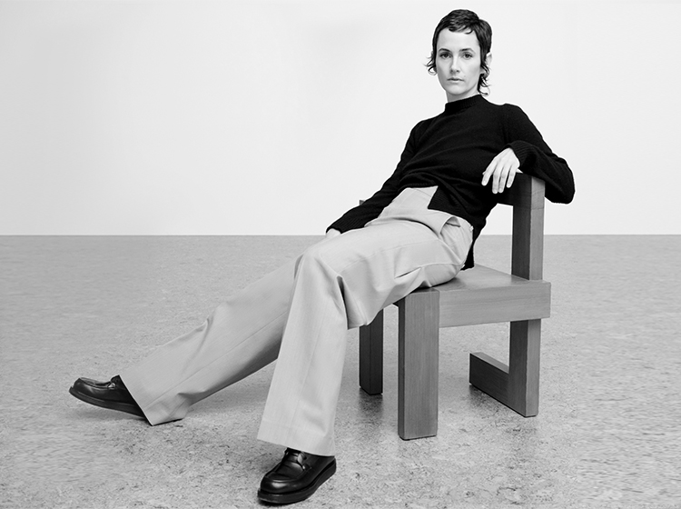Karla Welch casually sits on a wooden chair while she looks into the camera.
