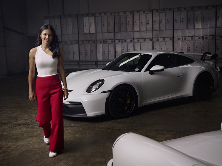 Emma Raducanu in locker room in front of white Porsche 911 GT3