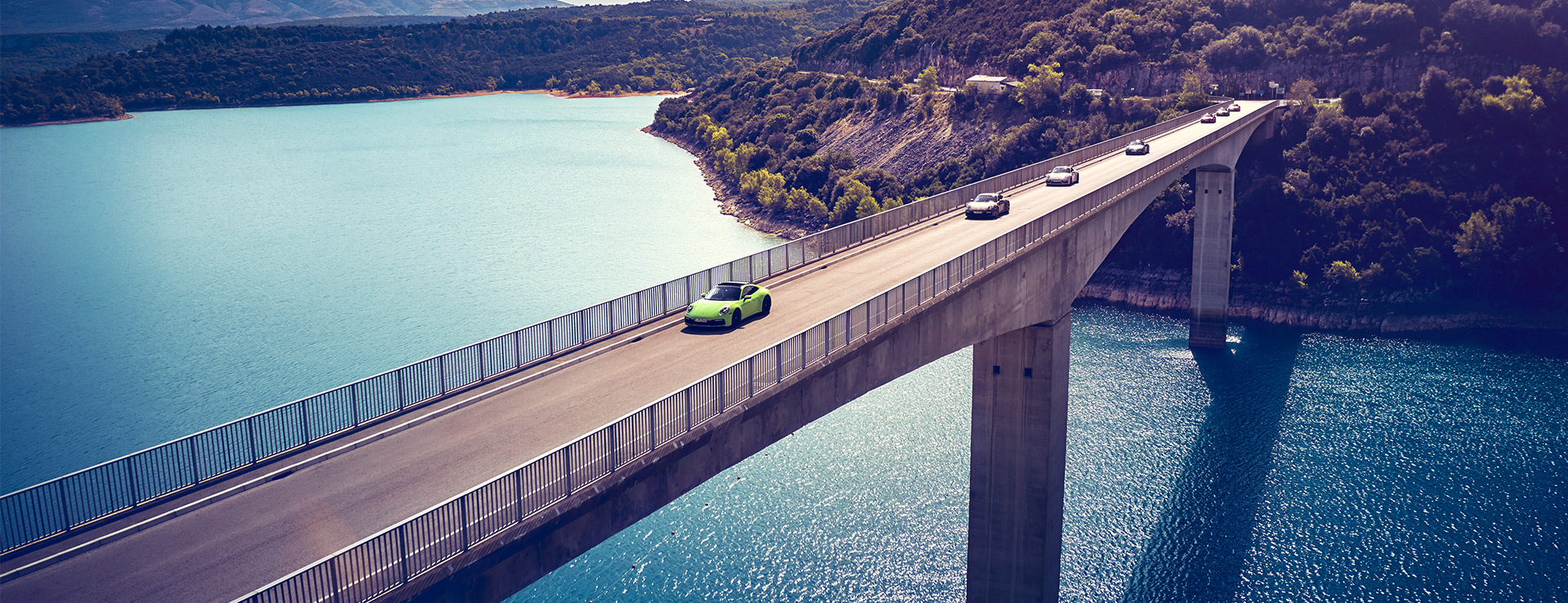 Porsche cars driving in convoy along a bridge