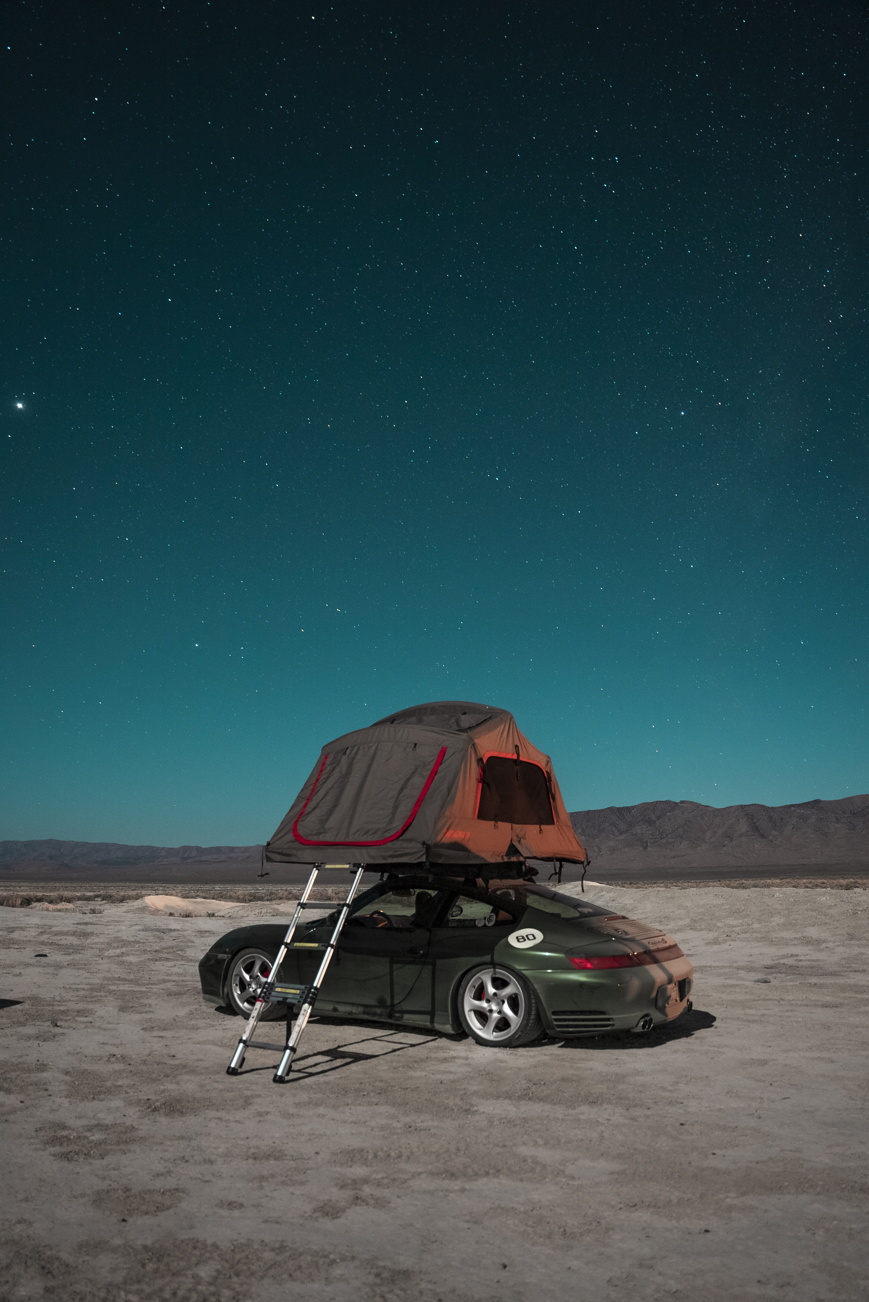 Porsche with roof tent in desert under starlit sky