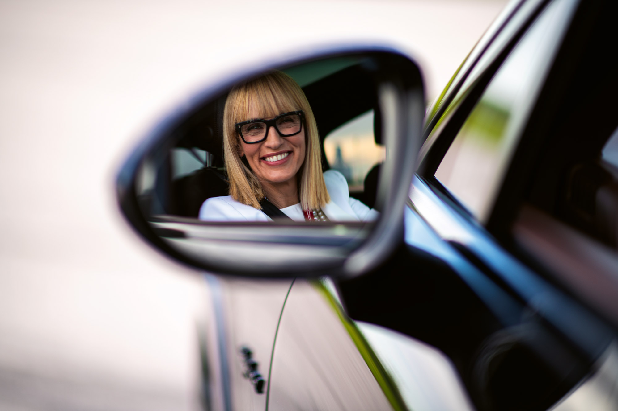 Blonde woman shown in door mirror of a Porsche