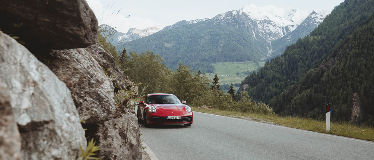 Red Porsche 911 drives on road in the Alps