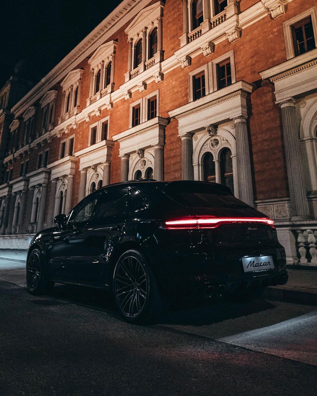 Black Porsche Macan outside lit-up building at night