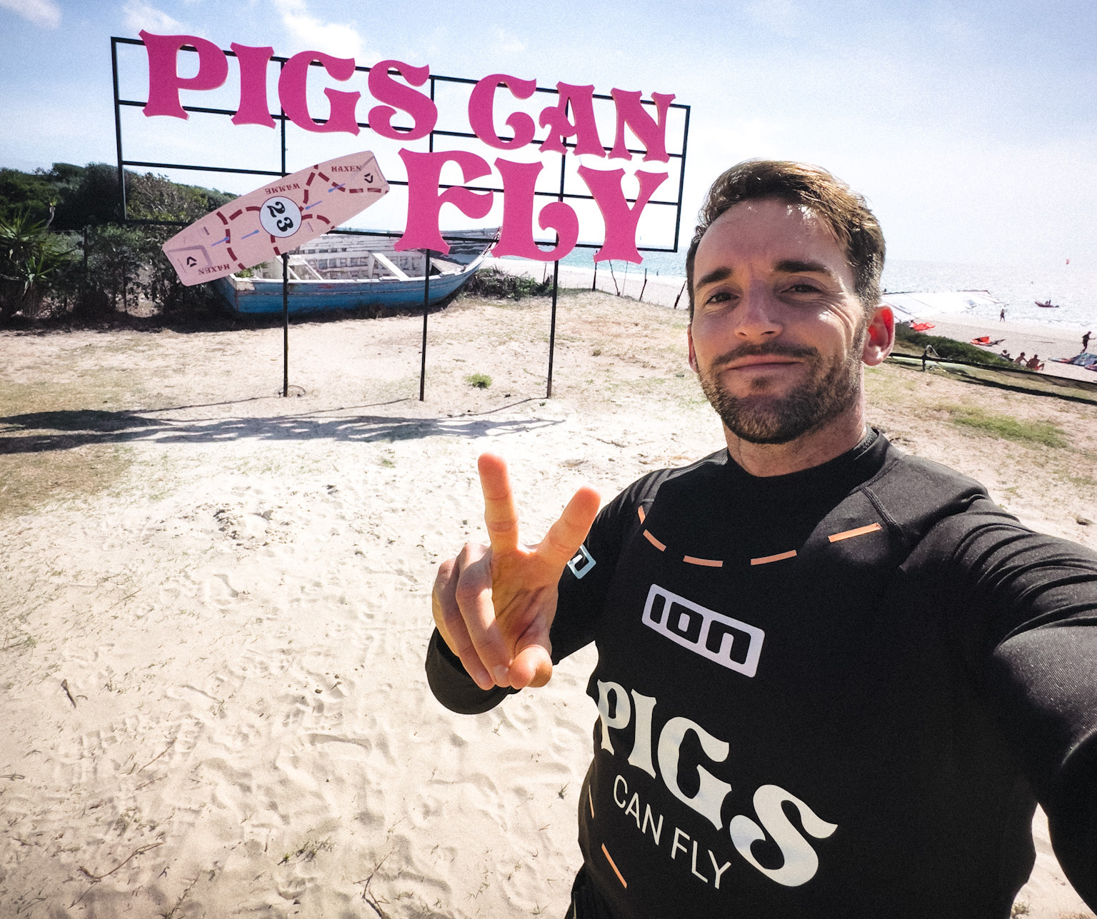 Man wearing wetsuit shoots victory sign on beach