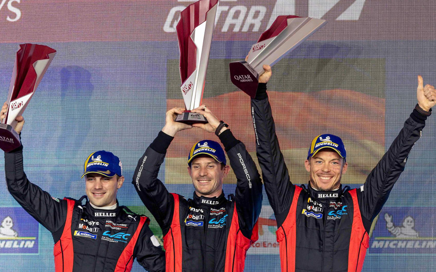 Three Porsche motor racing drivers wave trophies on podium