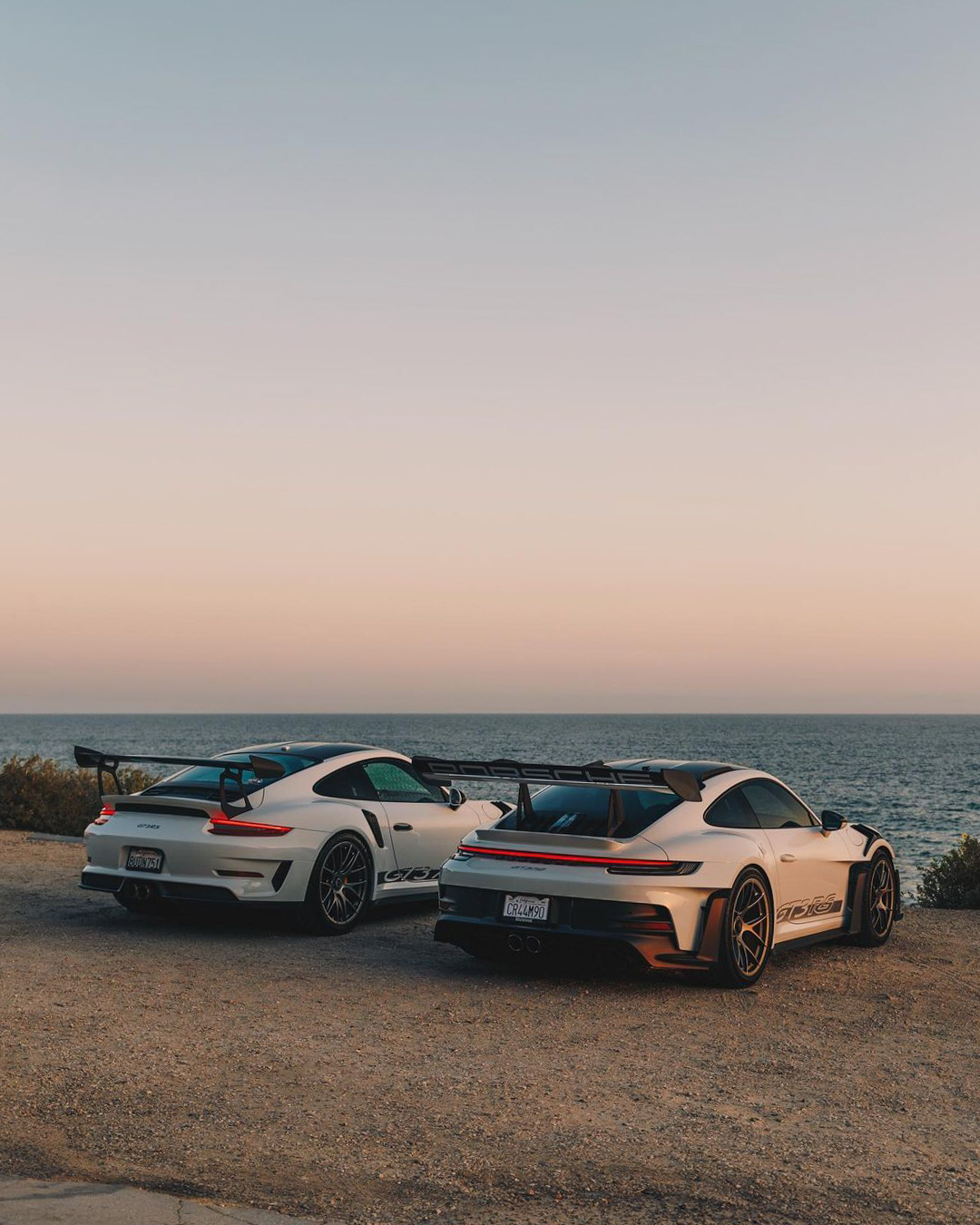 Two Porsche GT3 RS cars overlooking the ocean at sunset